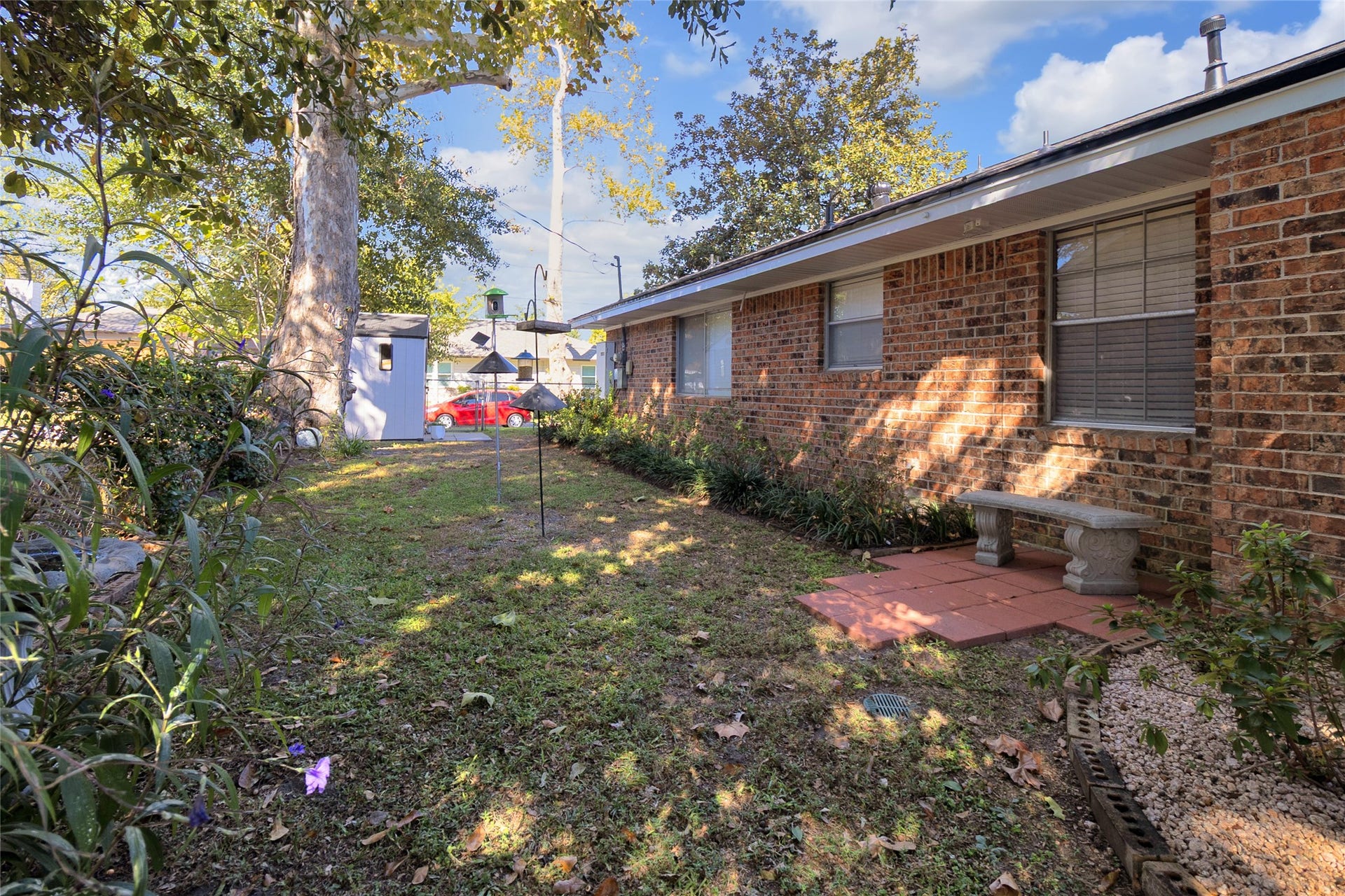 613 N Avenue F, Humble, TX 77338 Backyard oasis with mature trees, lush landscaping, and a cozy brick patio perfect for relaxing outdoors.