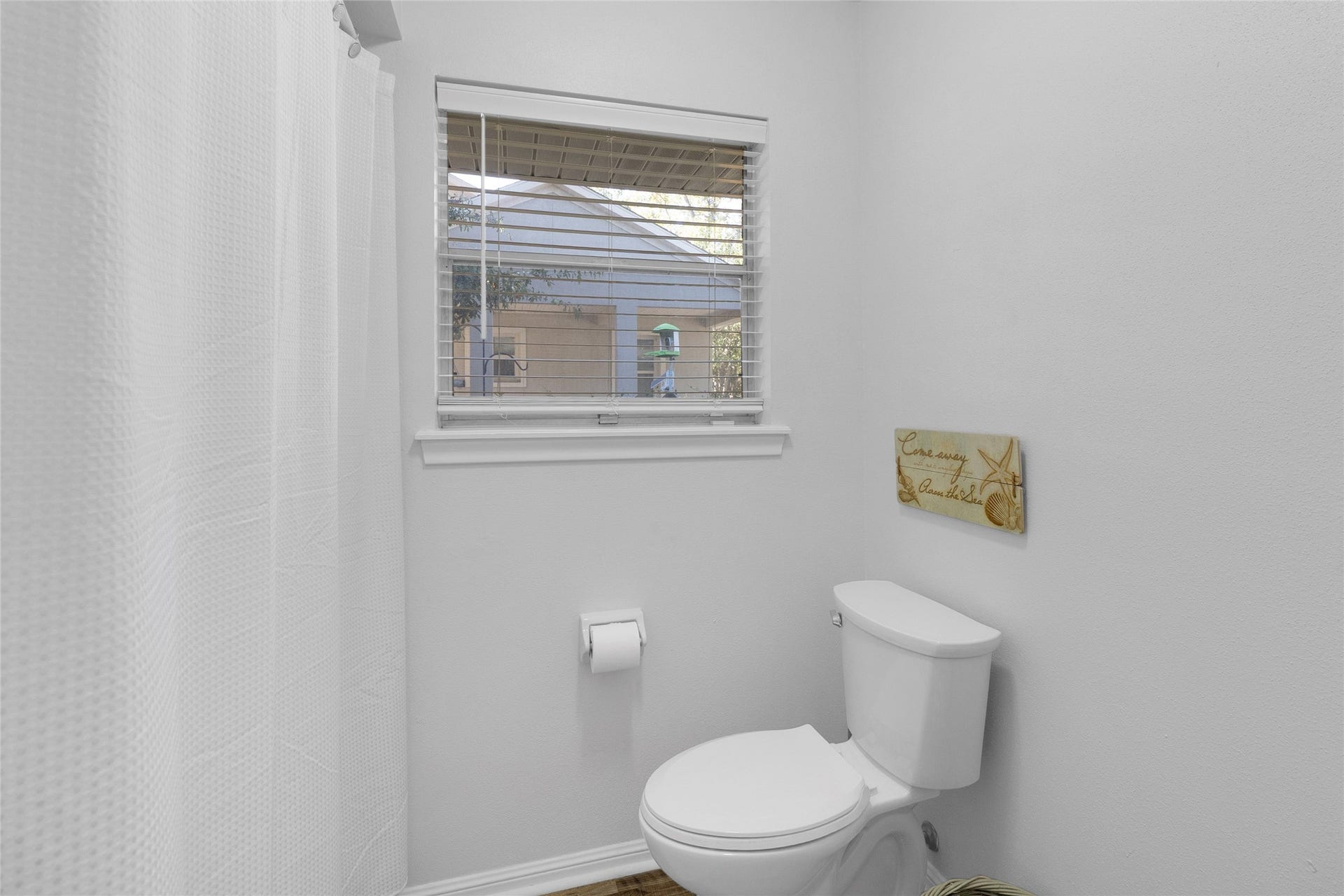 613 N Avenue F, Humble, TX 77338 Bright and cozy bathroom featuring a window for natural light, a modern toilet, and a shower with a clean, white curtain.