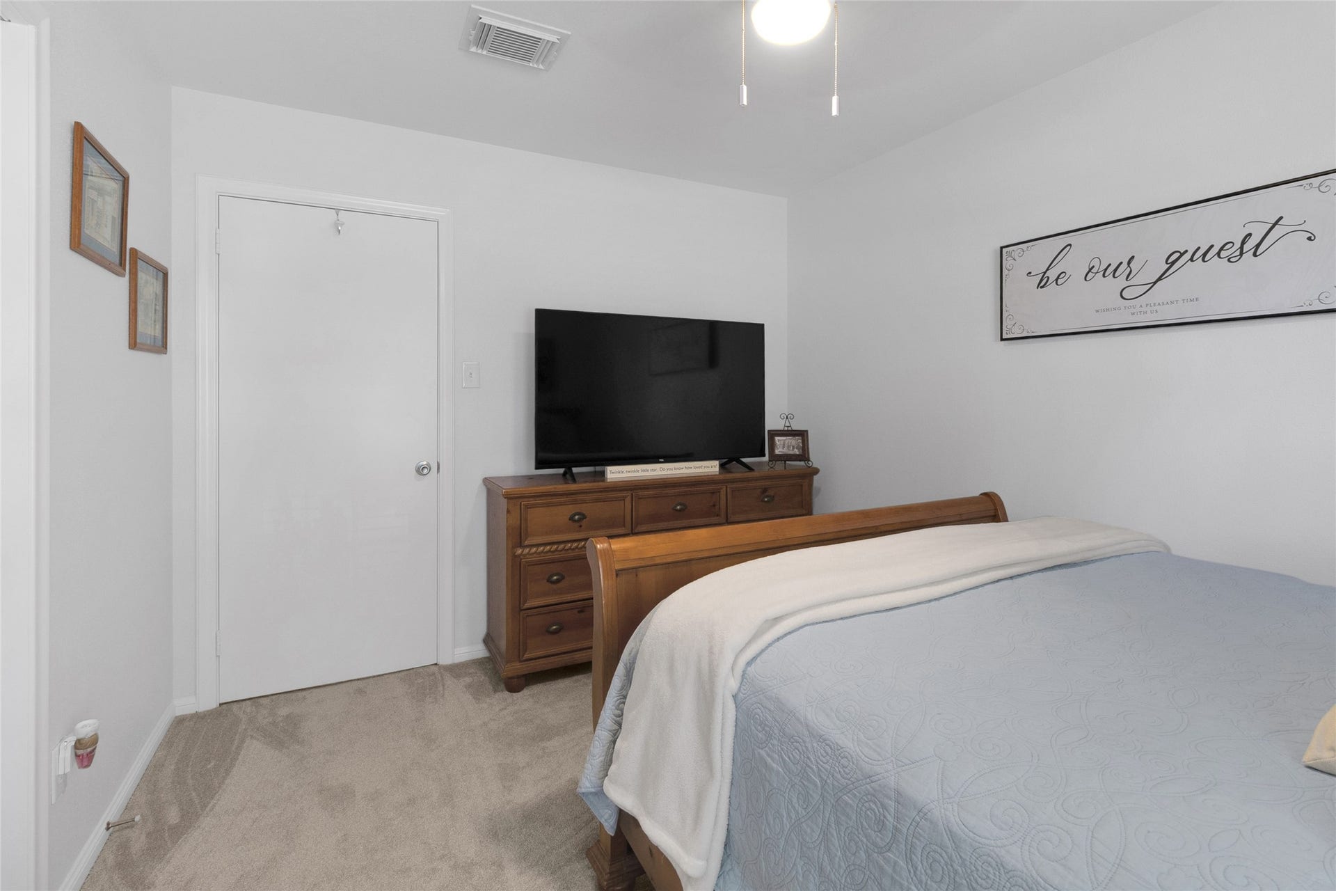 613 N Avenue F, Humble, TX 77338 Generous bedroom with a plush carpet, stylish wooden furniture, and a welcoming wall sign, perfect for relaxation.