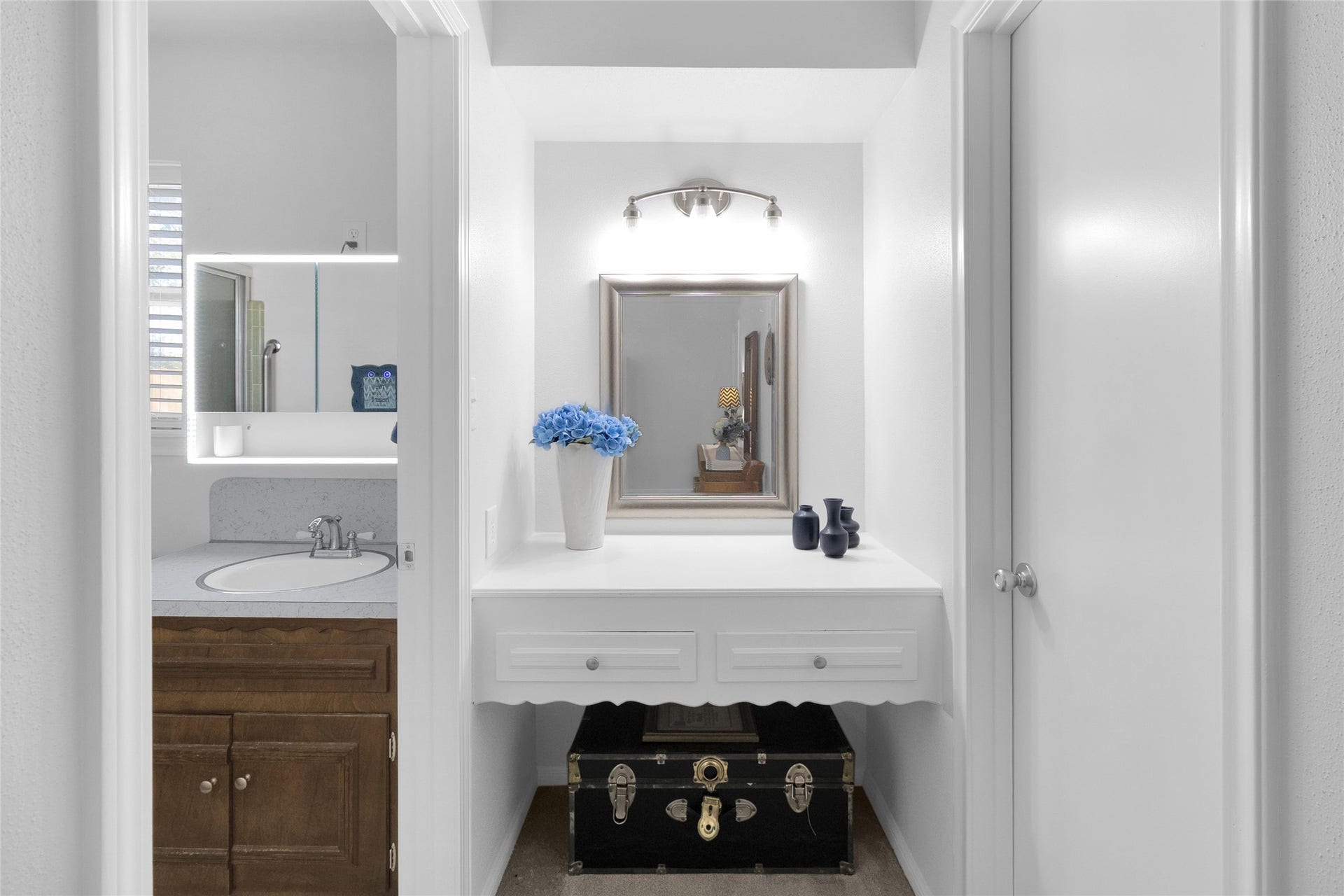 613 N Avenue F, Humble, TX 77338 Charming vanity area with elegant lighting and a built-in mirror, adjacent to a well-appointed bathroom featuring a stylish sink and wood cabinetry.