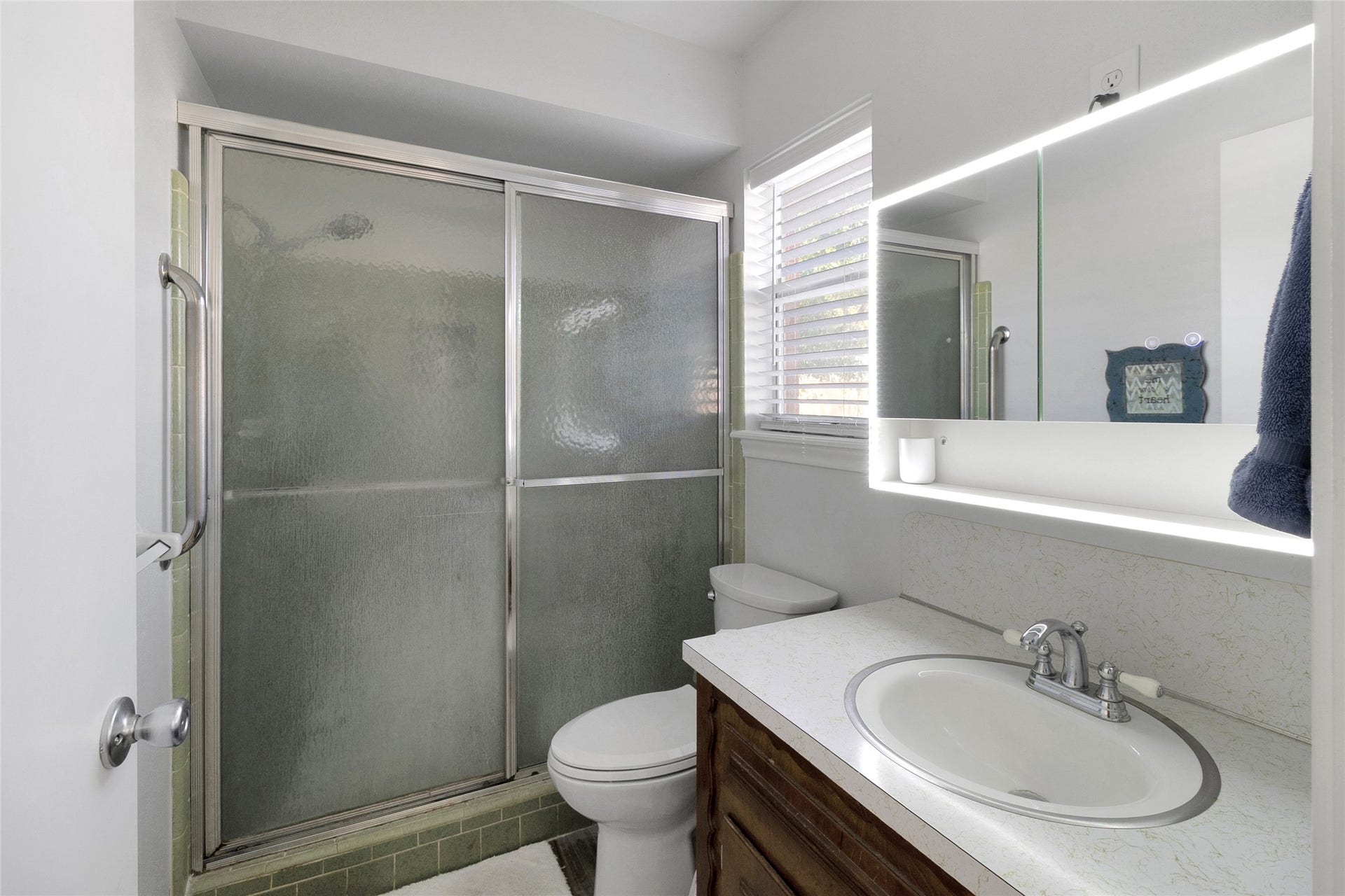 613 N Avenue F, Humble, TX 77338 Bright bathroom featuring a shower with sliding glass doors, sleek vanity, and an illuminated mirror, creating a clean and inviting space.