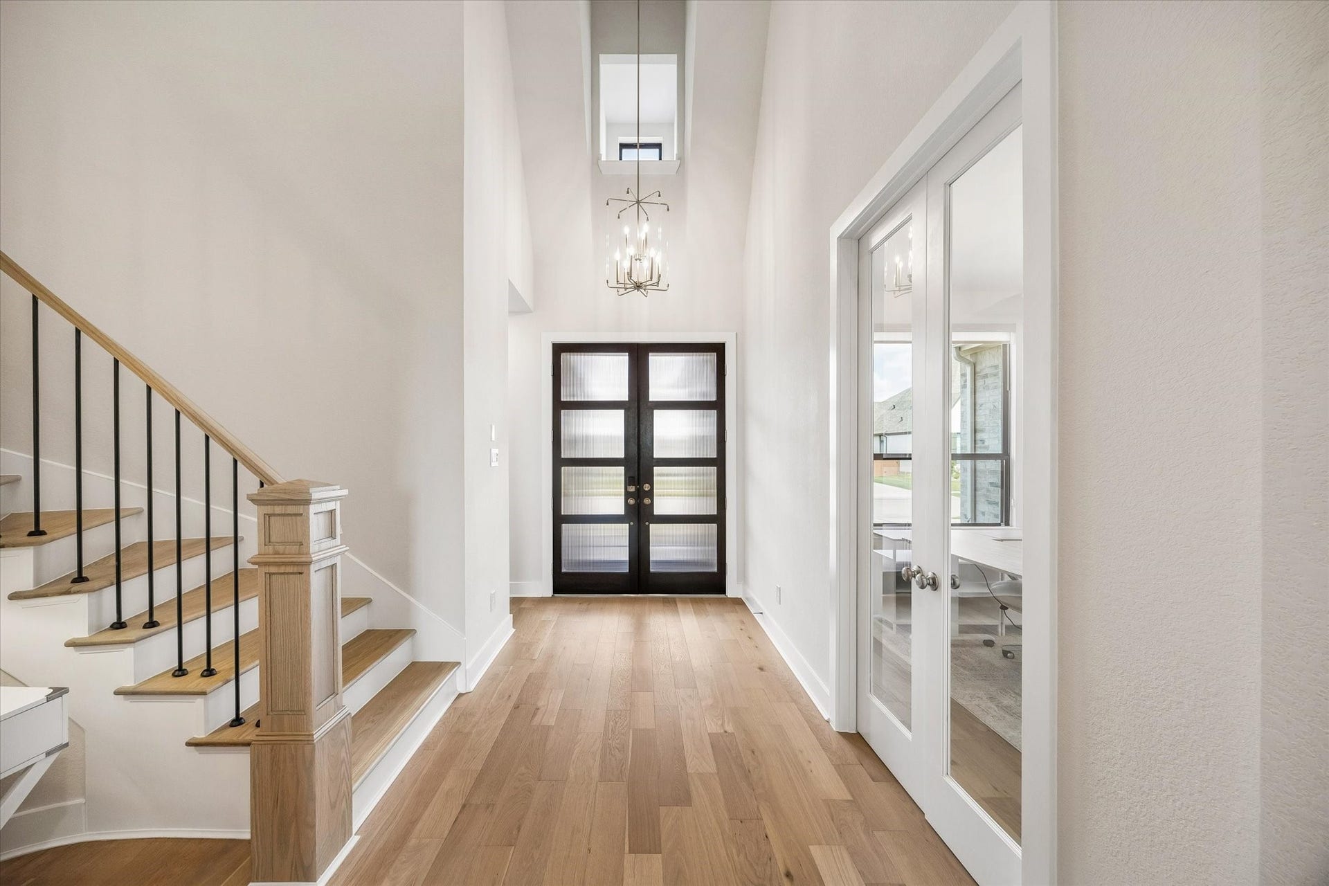 TWO-STORY FOYER WITH A STATEMENT CHANDELIER, MODERN DOUBLE FRONT DOORS, WOOD FLOORING, AND DIRECT ACCESS TO THE PRIVATE STUDY.