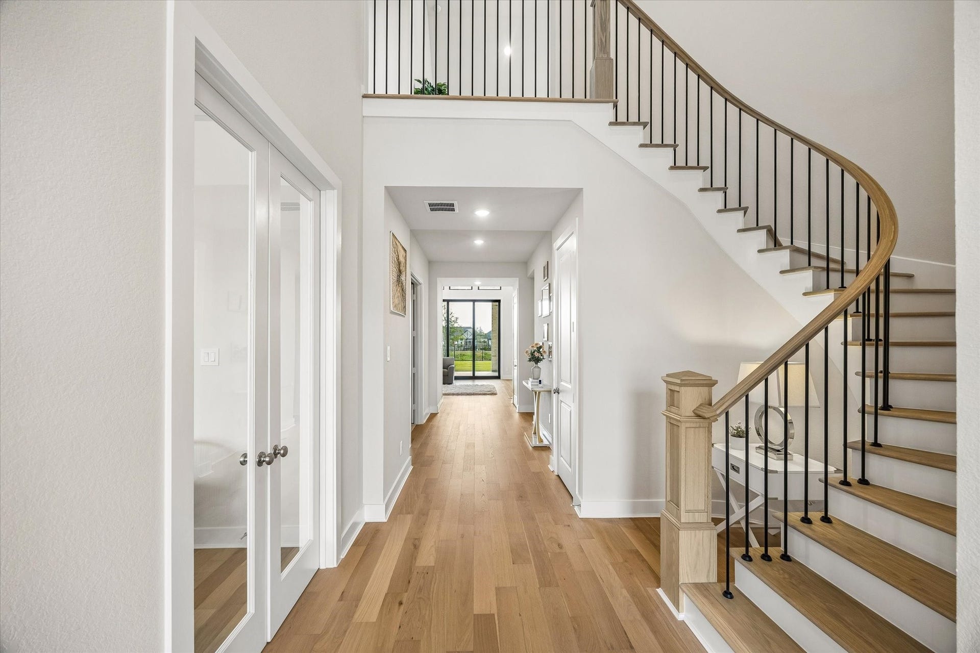 BRIGHT ENTRY HALL FEATURES WIDE-PLANK WOOD FLOORING AND A CURVED STAIRCASE WITH WOOD TREADS AND BLACK IRON BALUSTERS.