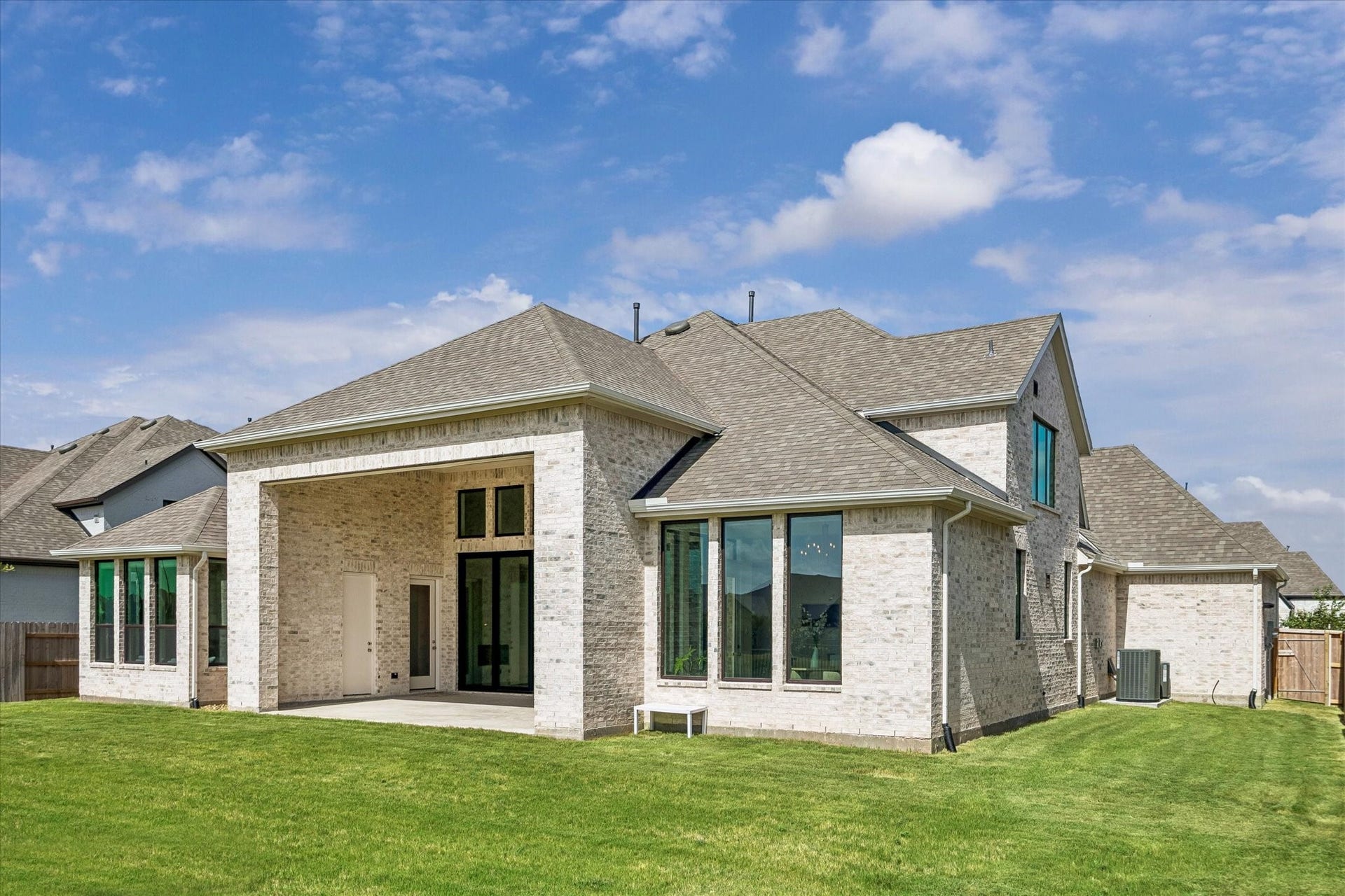 REAR EXTERIOR HIGHLIGHTS THE LIGHT BRICK FINISH, COVERED PATIO, TALL WINDOWS, AND LARGE BACKYARD.  ONE OF THE DOORS ON THE PATIO LEADS TO A THIRD POWDER BATH - PERFECT FOR A POOL BATH IF YOU CHOOSE TO BUILD ONE IN THE FUTURE!