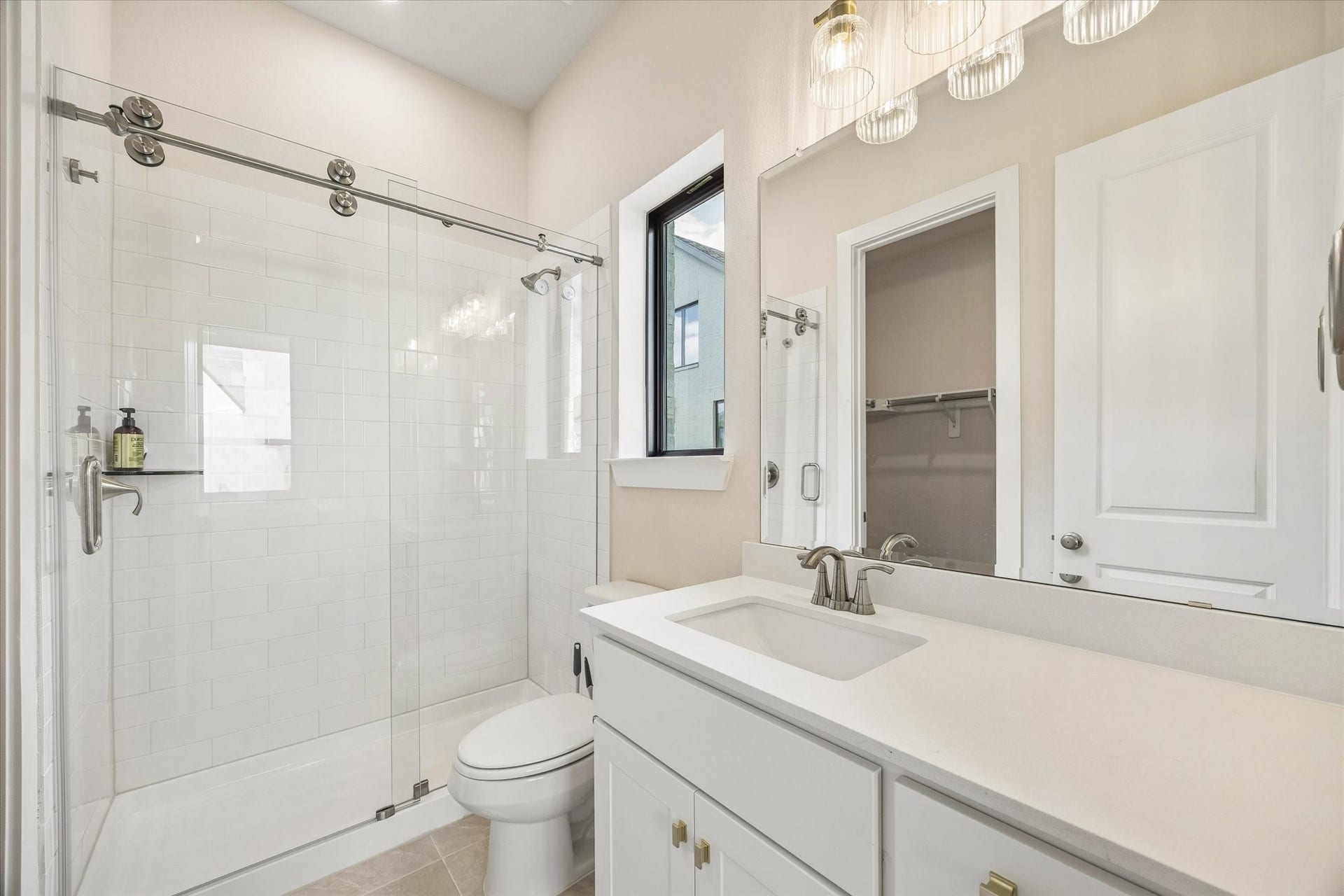 EN SUITE BATH INCLUDES A GLASS-ENCLOSED SHOWER WITH SUBWAY TILE, QUARTZ COUNTERTOP, LARGE MIRROR, AND A WALK-IN CLOSET.