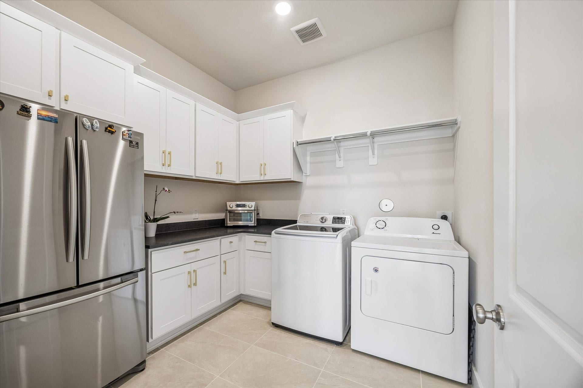 LARGE UTILITY ROOM OFFERS EXTENSIVE CABINET STORAGE, COUNTER SPACE, TILE FLOORING, AND ROOM FOR FULL-SIZE LAUNDRY APPLIANCES.