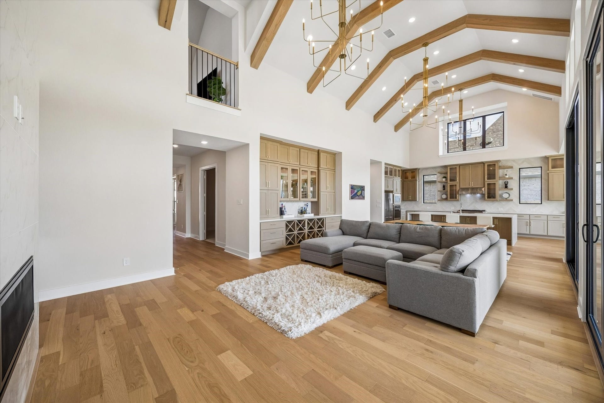 A WIDE VIEW OF THE FAMILY ROOM HIGHLIGHTS THE VAULTED CEILING, EXPOSED WOOD BEAMS, AND OPEN SIGHTLINES TO THE KITCHEN. LARGE GLASS DOORS AND HIGH WINDOWS FILL THE SPACE WITH LIGHT.