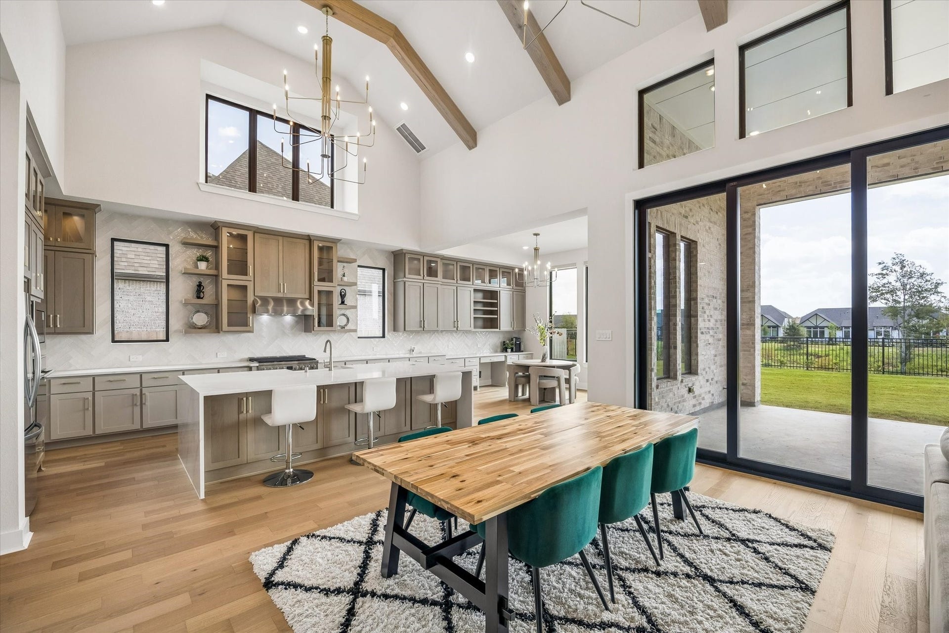 OPEN KITCHEN AND DINING AREA FEATURES SOARING CEILINGS, EXPOSED WOOD BEAMS, OVERSIZED WINDOWS, AND LARGE SLIDING GLASS DOORS OVERLOOKING THE BACKYARD.