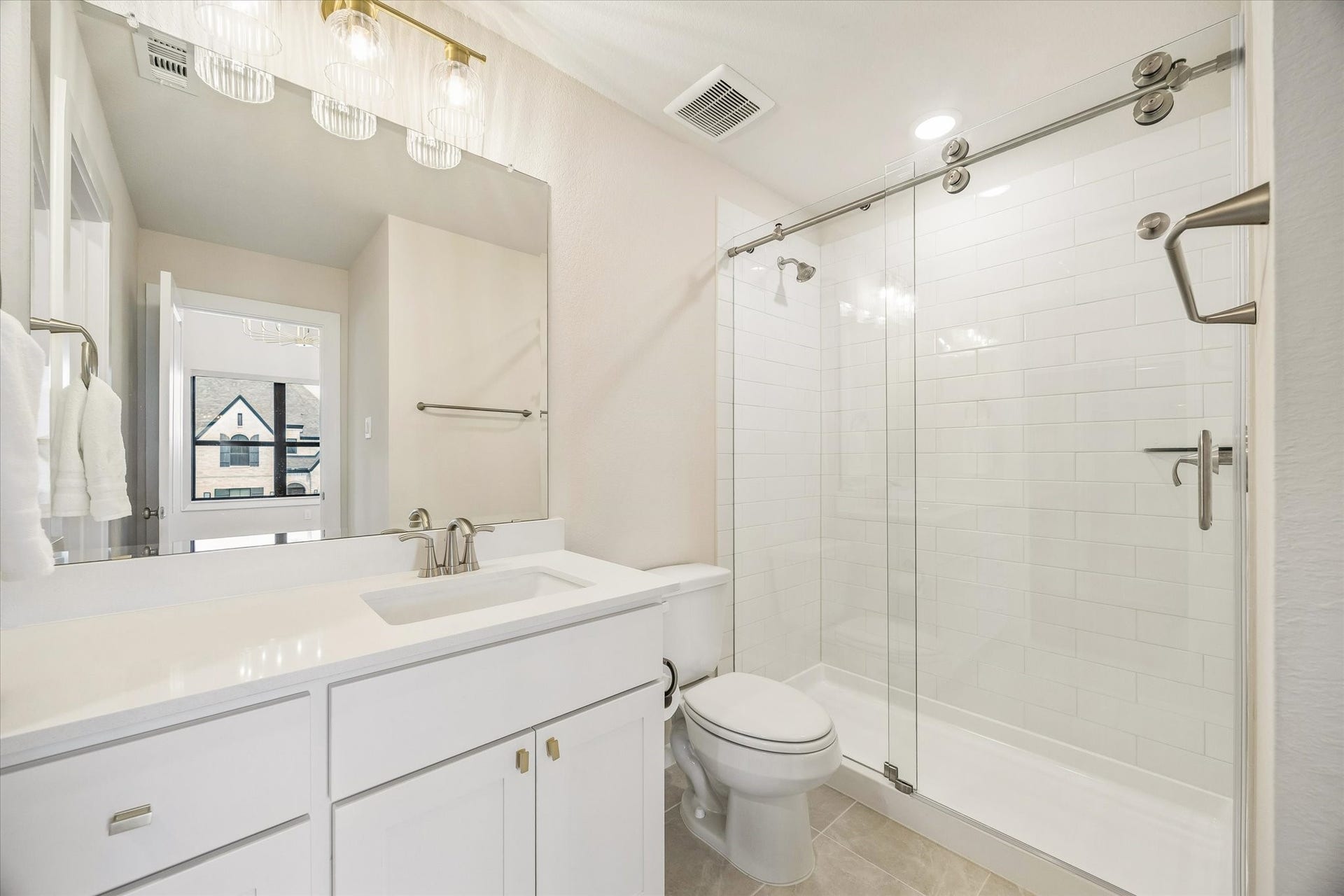 THIS SECONDARY BATH FEATURES A GLASS-ENCLOSED SHOWER, WHITE SUBWAY TILE, QUARTZ VANITY, AND CLEAN NEUTRAL FINISHES.