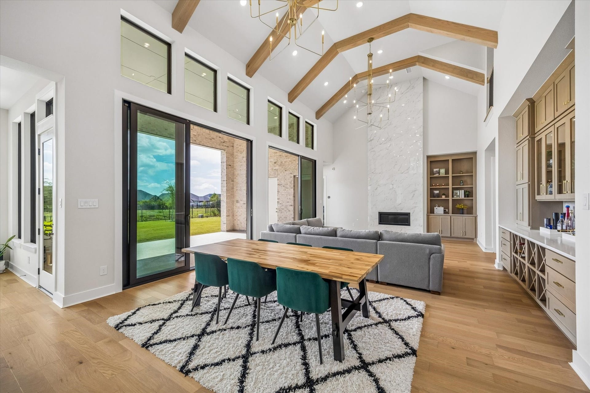 THE MAIN LIVING AREA SHOWCASES SOARING CEILINGS, EXPOSED WOOD BEAMS, AND OVERSIZED SLIDING GLASS DOORS. A FLOOR-TO-CEILING FIREPLACE WALL AND BUILT-IN SHELVING CREATE A STRONG FOCAL POINT.