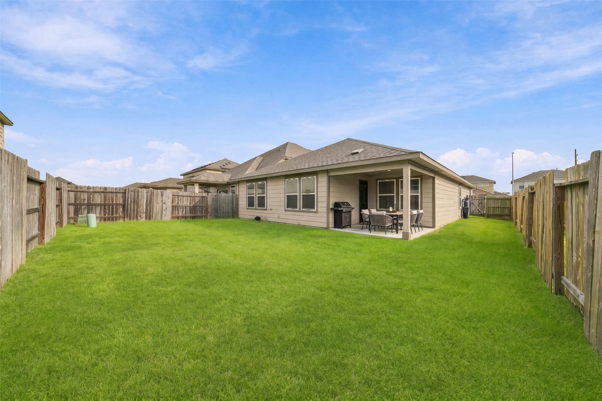 903 Pismo Lane, Rosharon, TX 77583 This photo captures a wide, eye-level, daytime outdoor view of a spacious residential backyard. The yard is entirely covered in a well maintained lush, vibrant green grass lawn.