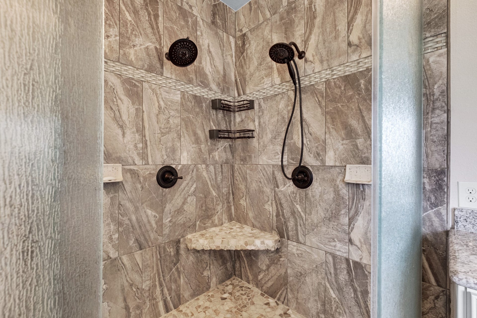 440 Old Orchard Court, Dickinson, TX 77539 The walk-in shower is finished floor to ceiling in stone-look tile with dual shower heads, a handheld on slide bar, corner seat, and pebble mosaic floor.