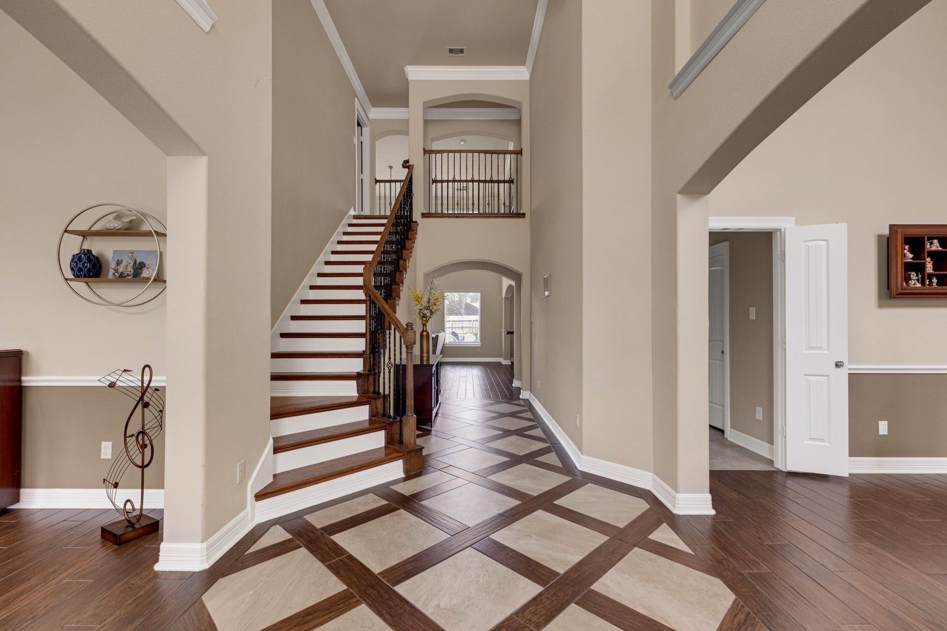 440 Old Orchard Court, Dickinson, TX 77539 Step inside to a two-story foyer laid in a harlequin inlay - travertine set on point, ribboned in mahogany wood tile - with a hardwood staircase and wrought-iron balusters climbing to the railed catwalk above, crown molding and chair rail carrying the formality down the hall.