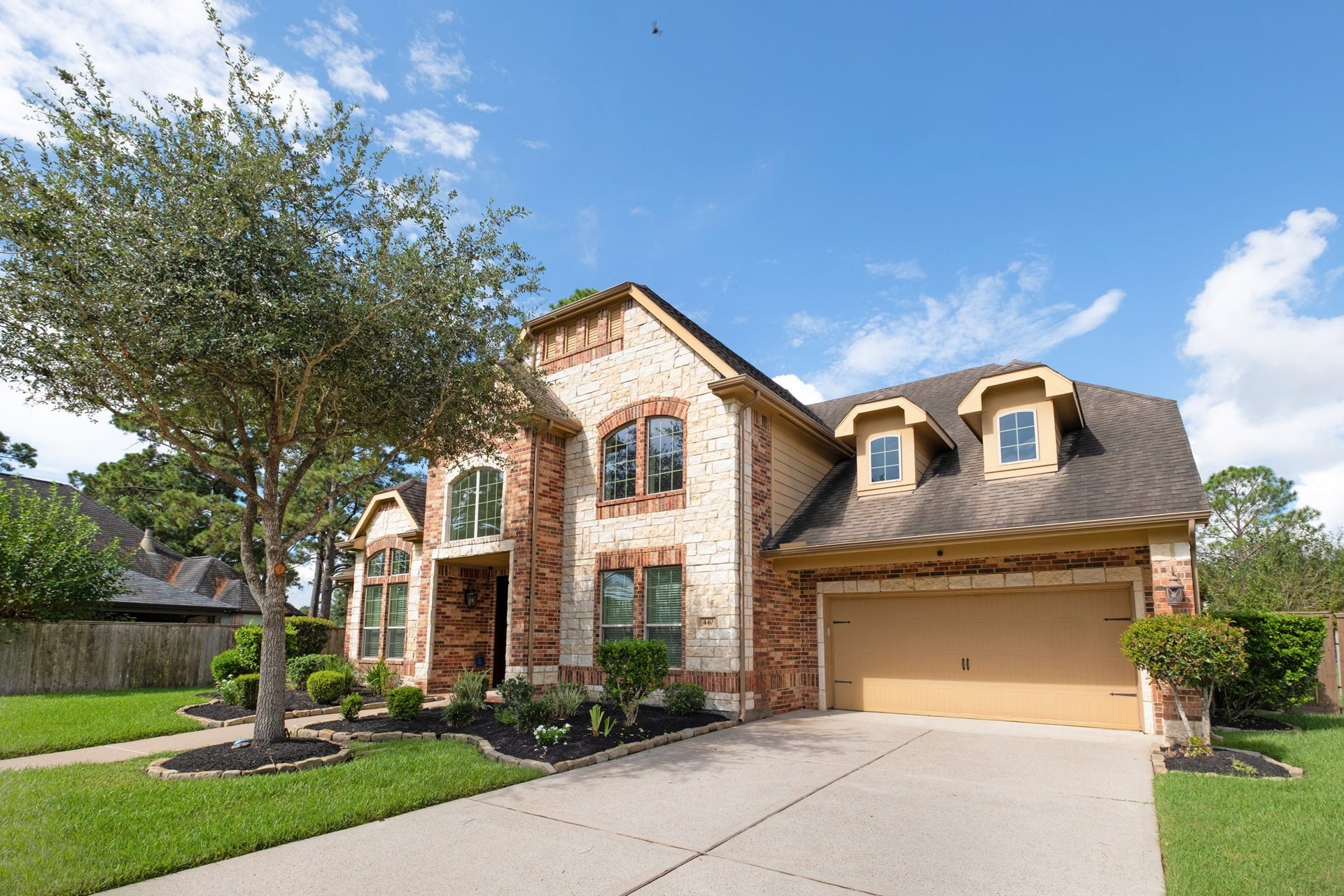 440 Old Orchard Court, Dickinson, TX 77539 From the drive side you see the full massing: dormered roofline, brick-and-stone bay, and a wide approach that keeps parking off the cul-de-sac.