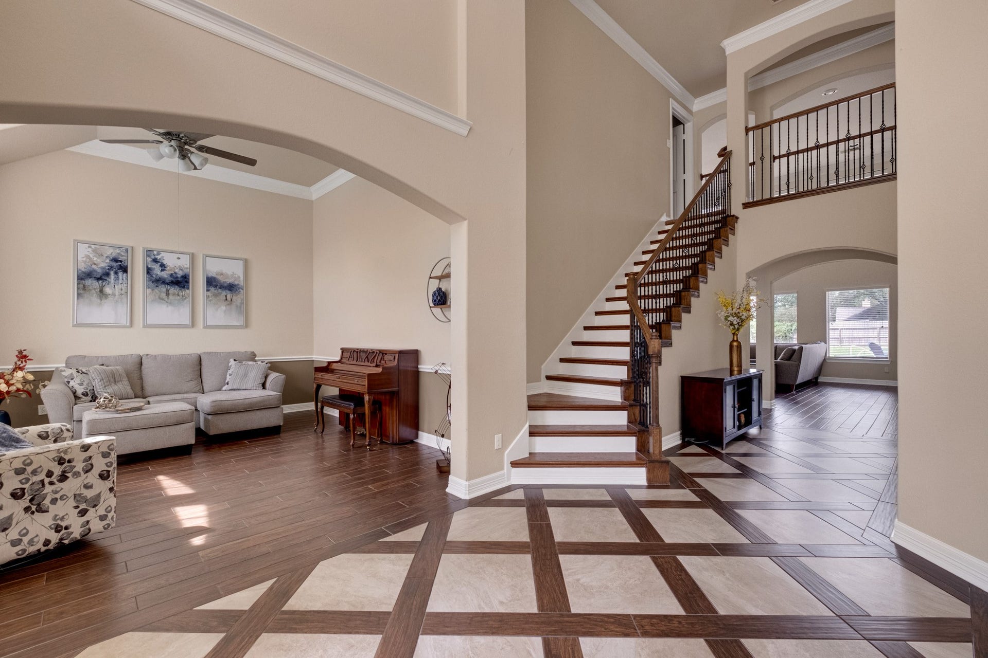 440 Old Orchard Court, Dickinson, TX 77539 The foyer opens both directions at once - formal living through a soft arch to the left, the staircase and iron-railed catwalk to the right, and inlaid tile drawing the eye straight through.