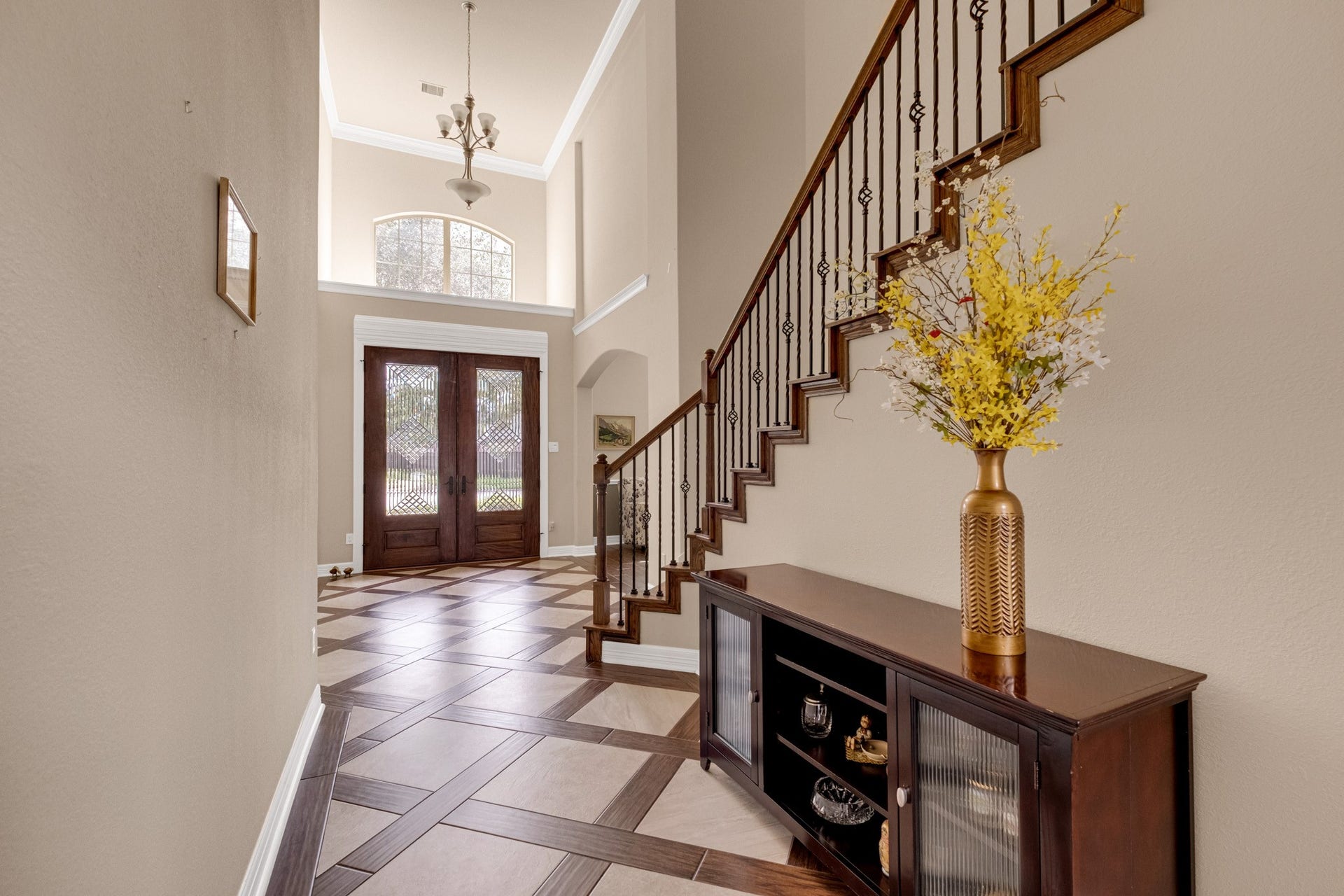 440 Old Orchard Court, Dickinson, TX 77539 Looking back toward the entry, an arched transom window floats above the doors and a chandelier hangs the full two stories, with the carved newel post and iron balusters anchoring the run.