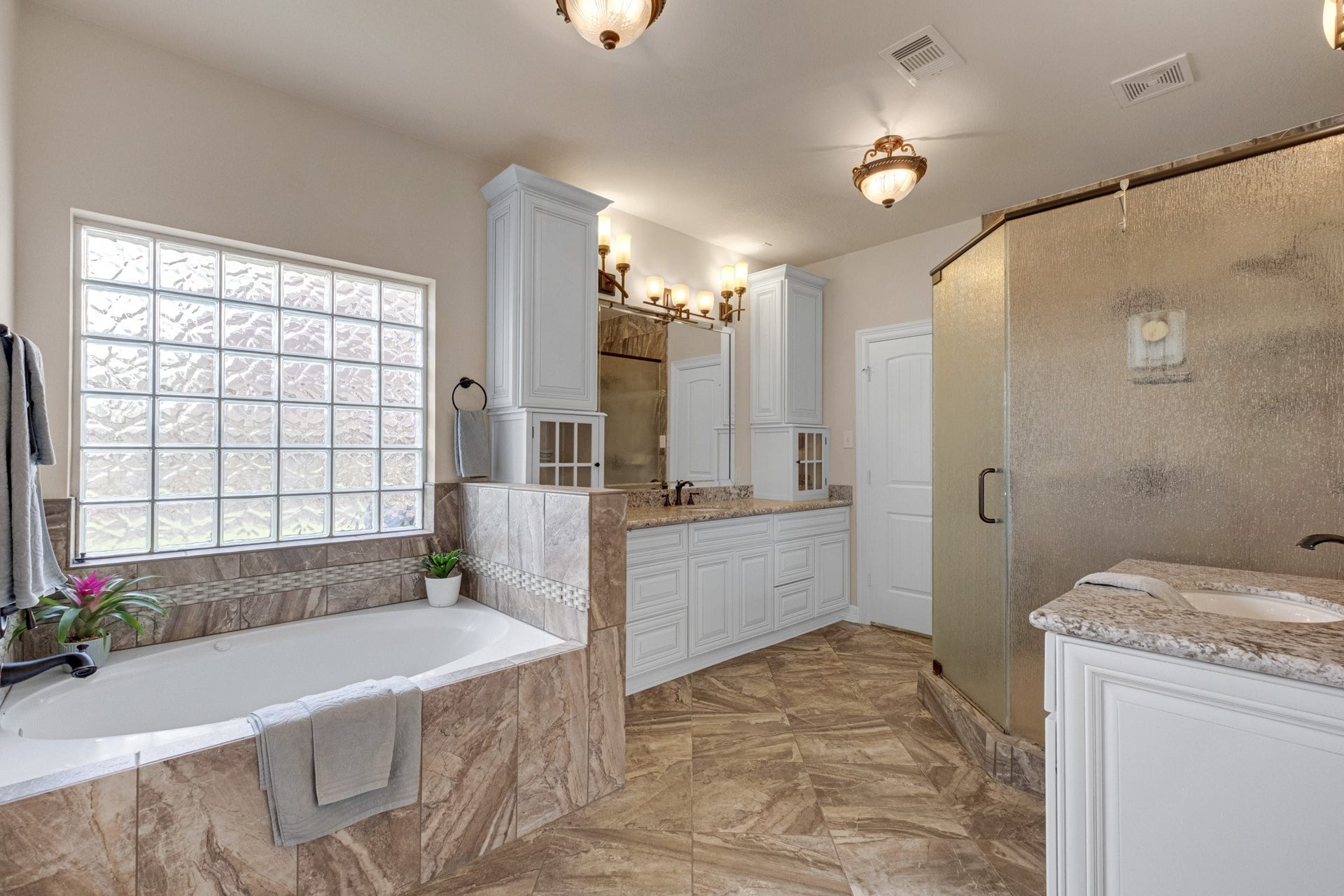 440 Old Orchard Court, Dickinson, TX 77539 The primary bath is a full retreat: a tiled garden tub beneath a glass block window, dual granite vanities with framed mirrors, and a separate glass-enclosed shower.