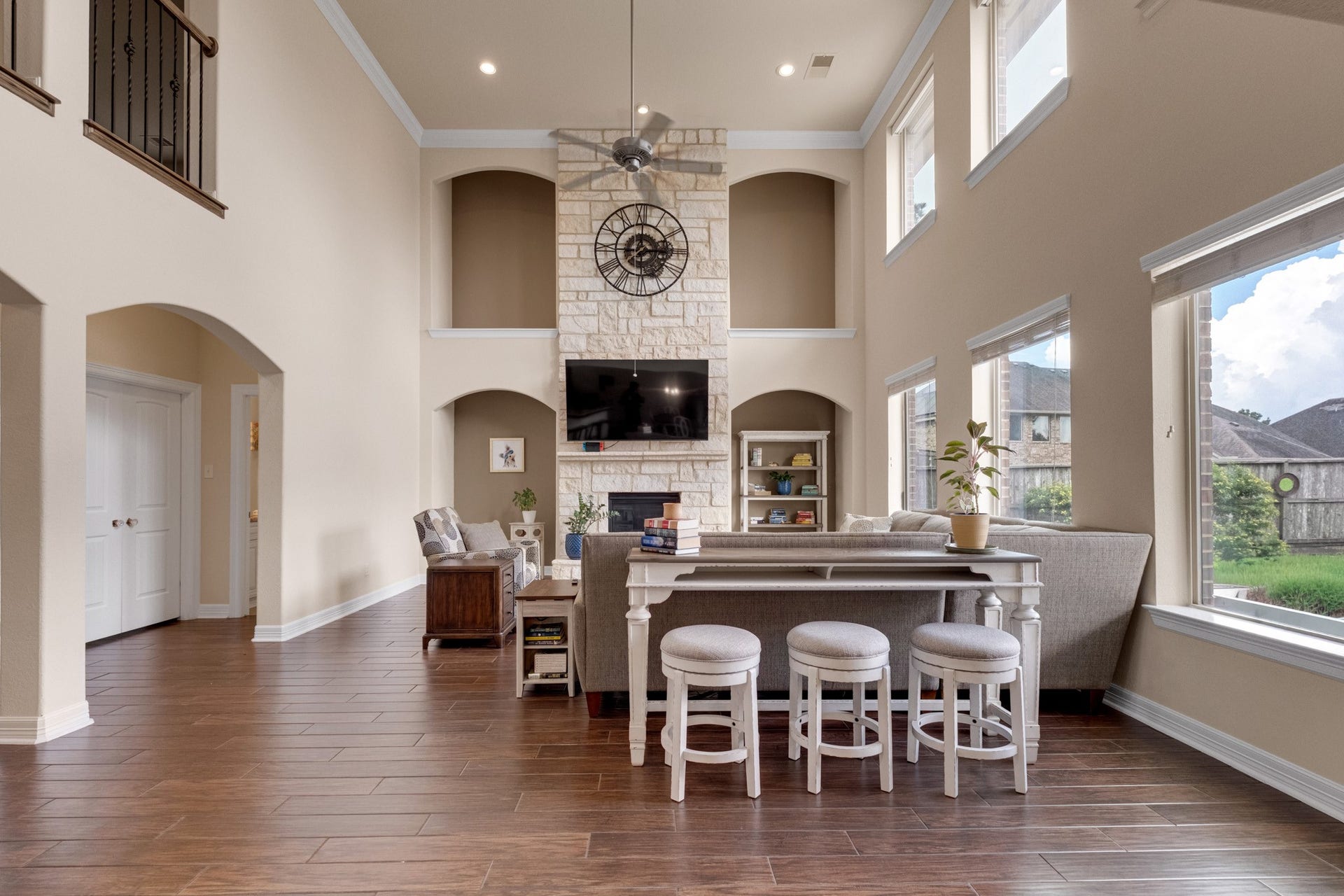 440 Old Orchard Court, Dickinson, TX 77539 The family room opens to soaring two-story ceilings, anchored by a floor-to-ceiling dry-stack Austin stone fireplace flanked by arched display niches, with a wall of windows pouring light across mahogany wood tile.