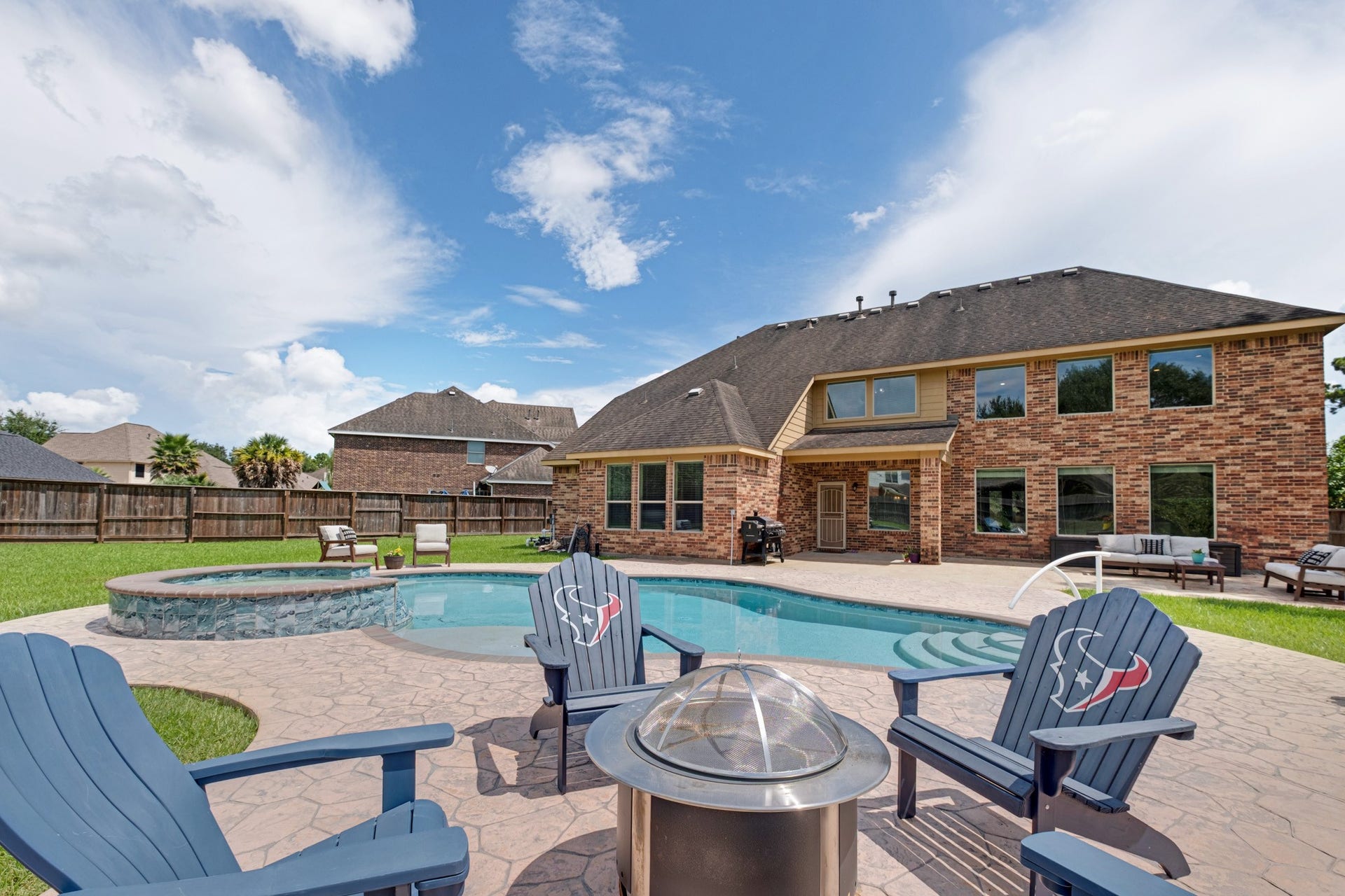 440 Old Orchard Court, Dickinson, TX 77539 The pool comes into its own from the deck - freeform water with a raised stone spa spilling in, a fire pit ring in stamped concrete, and the two-story brick elevation as the backdrop.