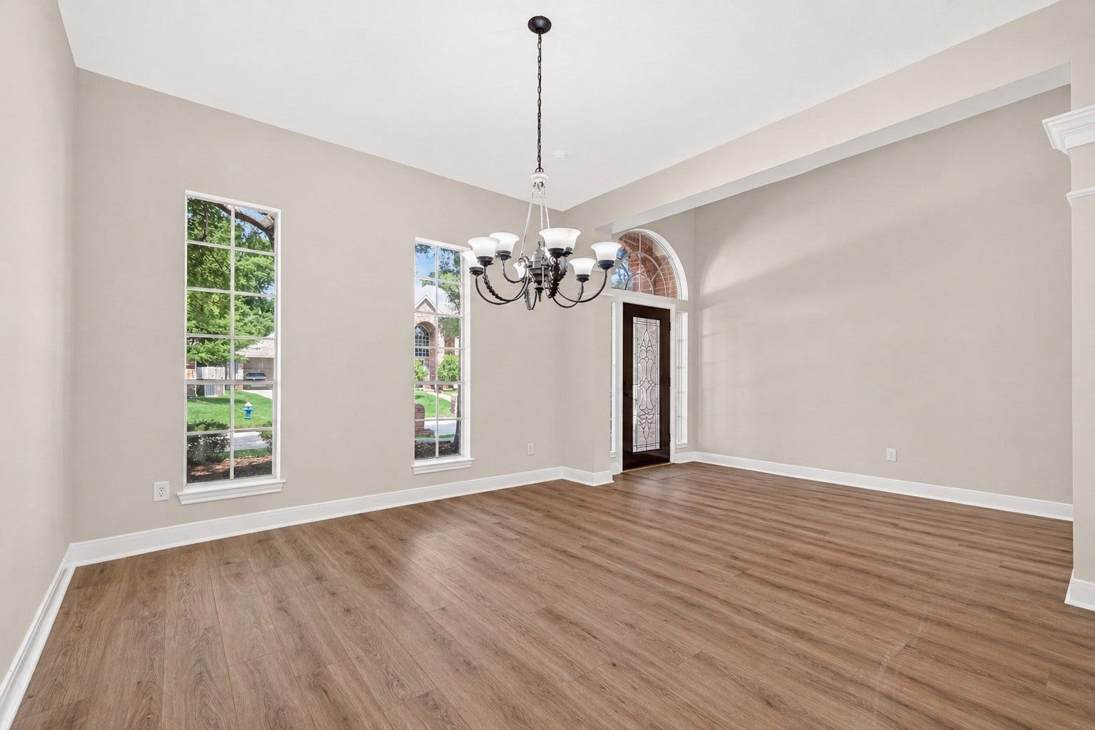 3610 Forest Row Drive, Houston, TX 77345 Bright and spacious room featuring elegant wood flooring, high ceilings, and a stylish chandelier, accented by large windows and a charming glass-paneled door.