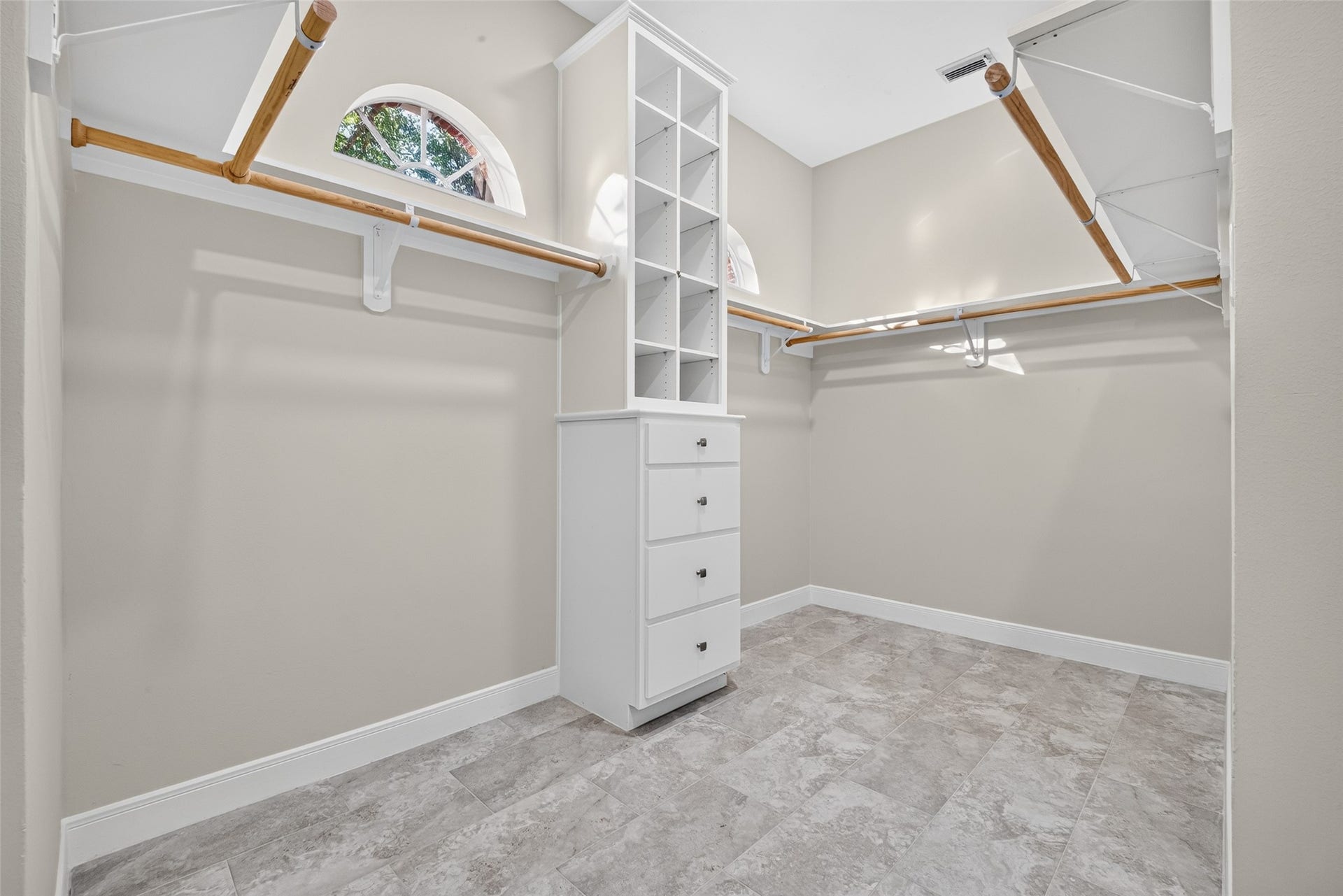 3610 Forest Row Drive, Houston, TX 77345 Spacious walk-in closet featuring wraparound hanging rods, overhead shelving, and a built-in drawer tower with open storage cubbies. Arched windows provide natural light.