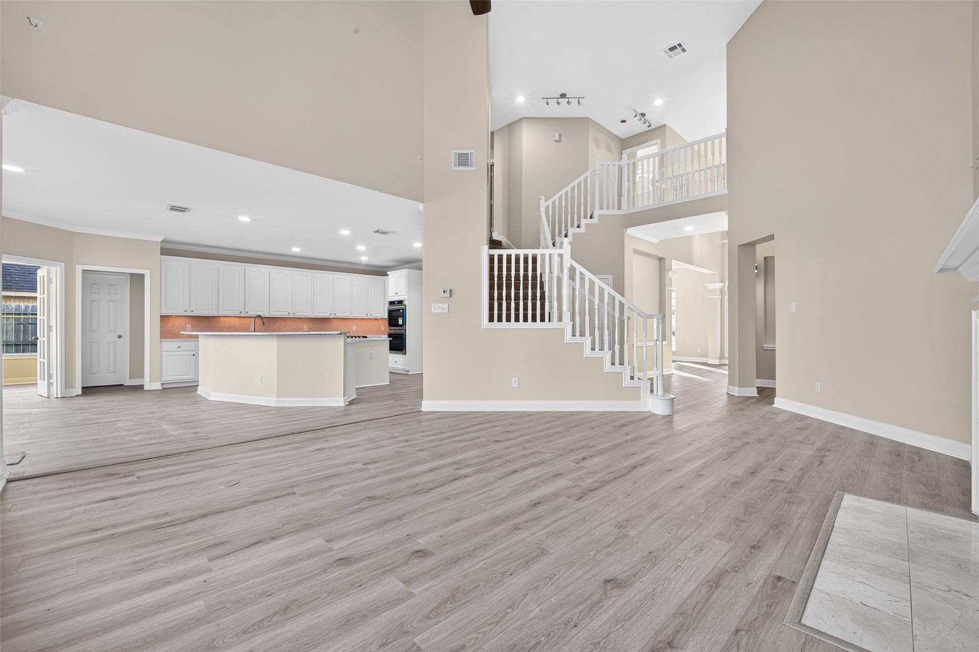 3610 Forest Row Drive, Houston, TX 77345 This living room view showcases the open kitchen connection, soaring ceilings, and staircase with white spindle railings. An overlooking upper landing adds architectural interest.