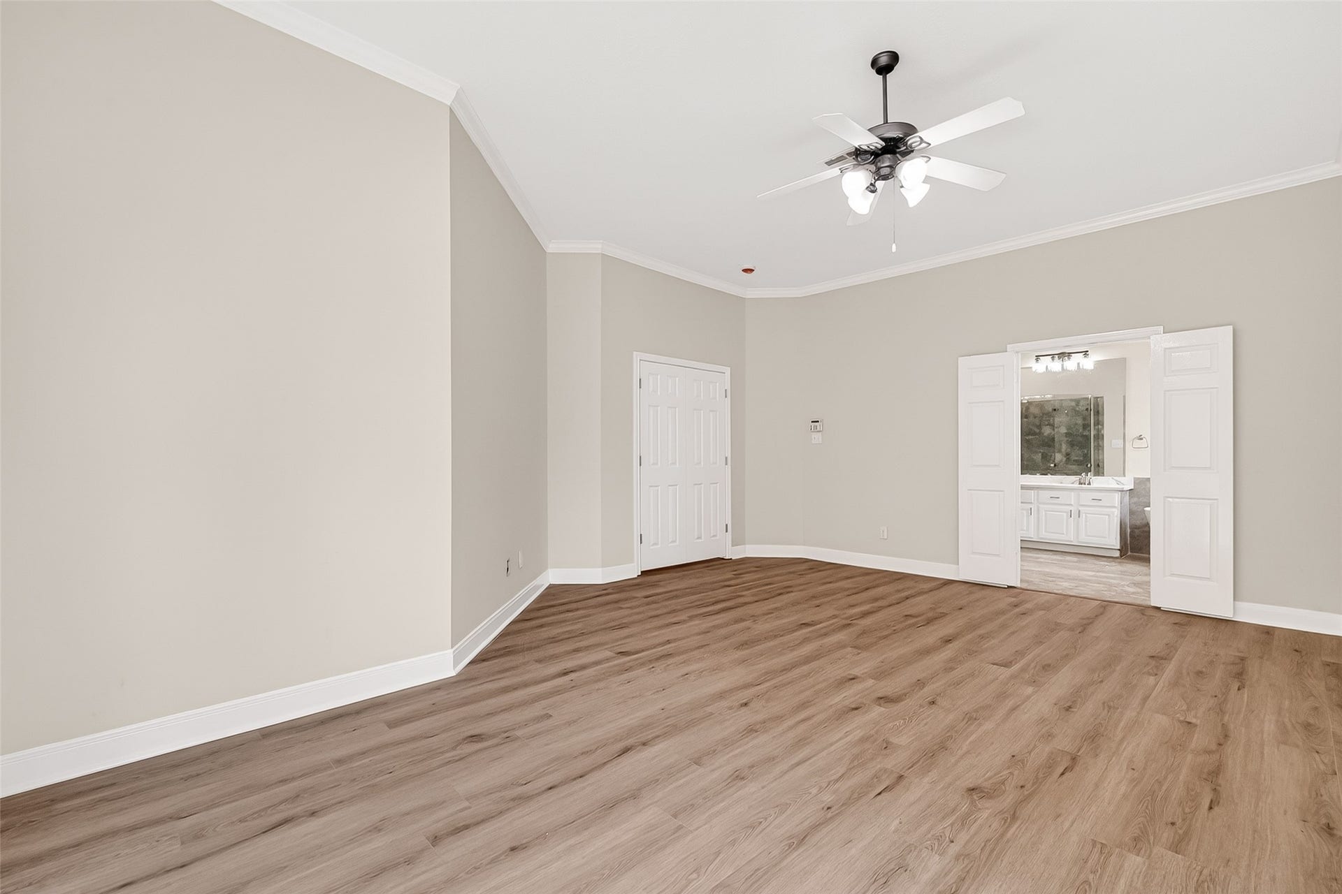 3610 Forest Row Drive, Houston, TX 77345 Spacious room with elegant wood flooring, neutral walls, and a ceiling fan, leading to a bright bathroom through double doors.