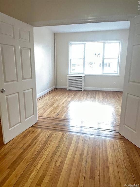 3138 103rd Street, #2ND FL, Corona, NY 11368 Hardwood flooring extending through an open doorway, white interior doors, and a window with a radiator below