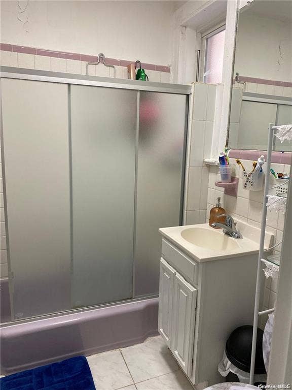 3138 103rd Street, #2ND FL, Corona, NY 11368 Tile flooring with white grout, a white vanity with a built-in sink and chrome faucet, and a shower/tub combination with sliding frosted glass doors