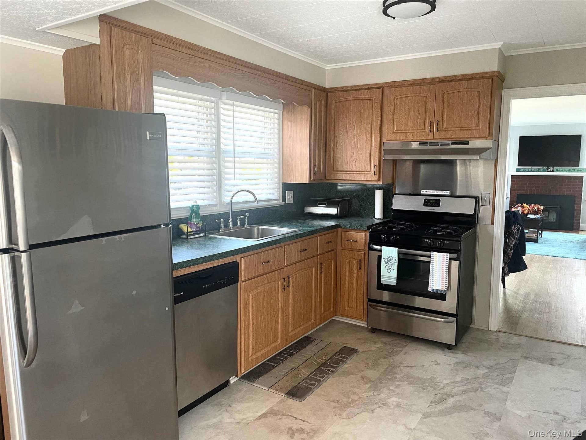 Kitchen with appliances with stainless steel finishes, brown cabinetry, dark countertops, ornamental molding, and under cabinet range hood