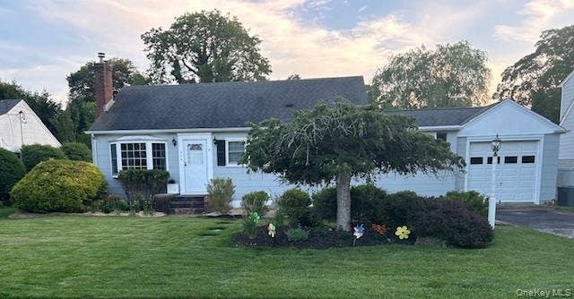 View of front of property featuring a lawn, an attached garage, a chimney, and driveway