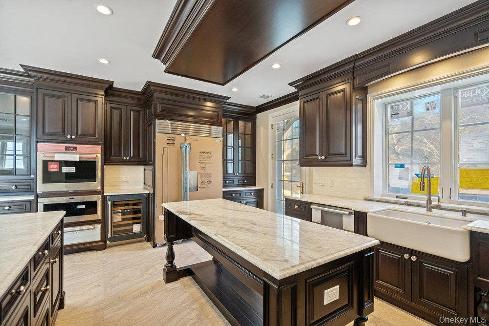 89 Mill River Road, Upper Brookville, NY 11771 Kitchen featuring dark brown cabinetry, stainless steel appliances, wine cooler, backsplash, and recessed lighting