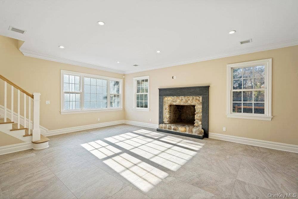 89 Mill River Road, Upper Brookville, NY 11771 Unfurnished living room featuring stairway, a stone fireplace, crown molding, and recessed lighting