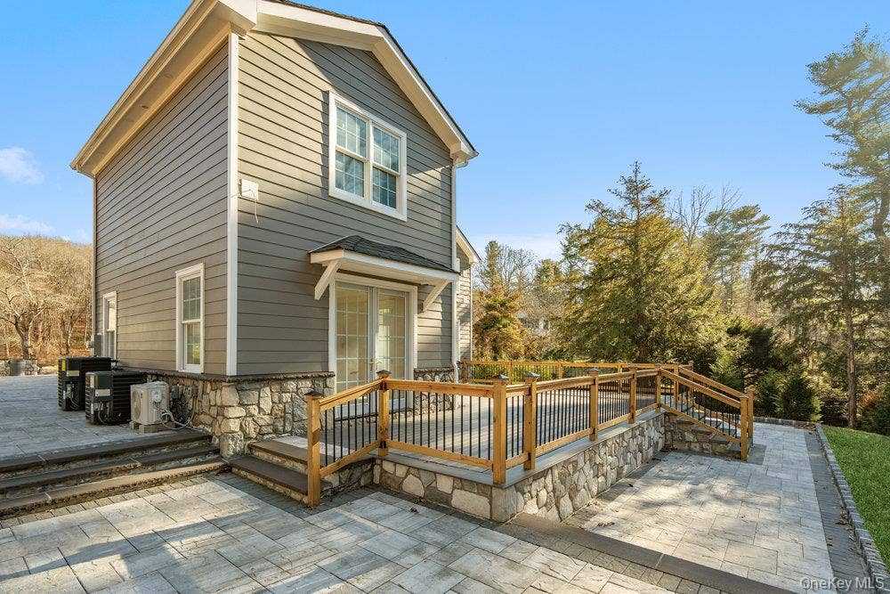 89 Mill River Road, Upper Brookville, NY 11771 Back of property featuring a wooden deck, stone siding, and a patio area