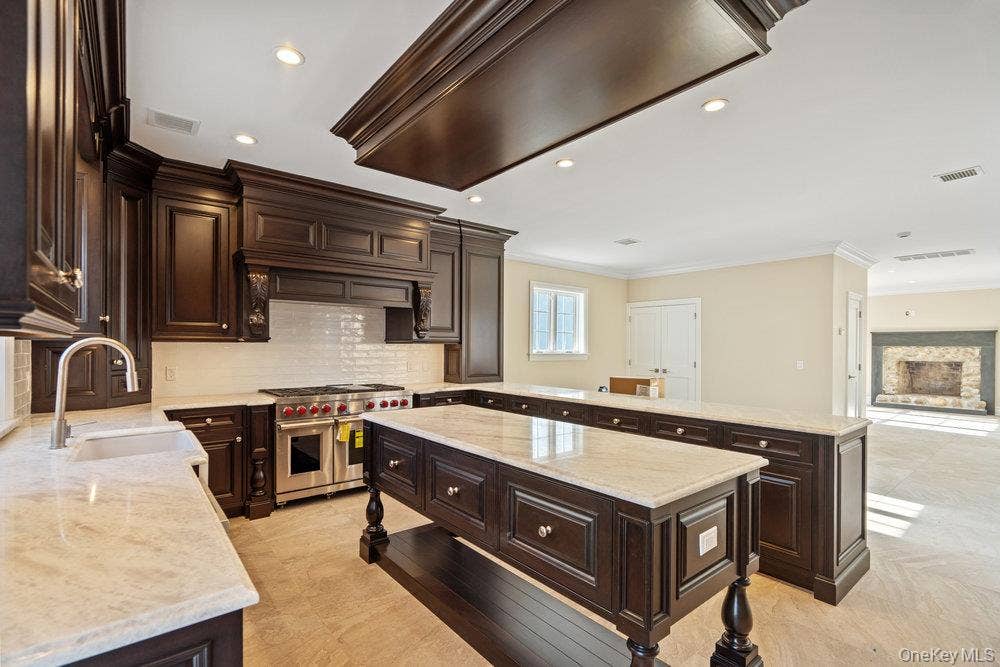 89 Mill River Road, Upper Brookville, NY 11771 Kitchen with dark brown cabinetry, a peninsula, open floor plan, double oven range, and crown molding