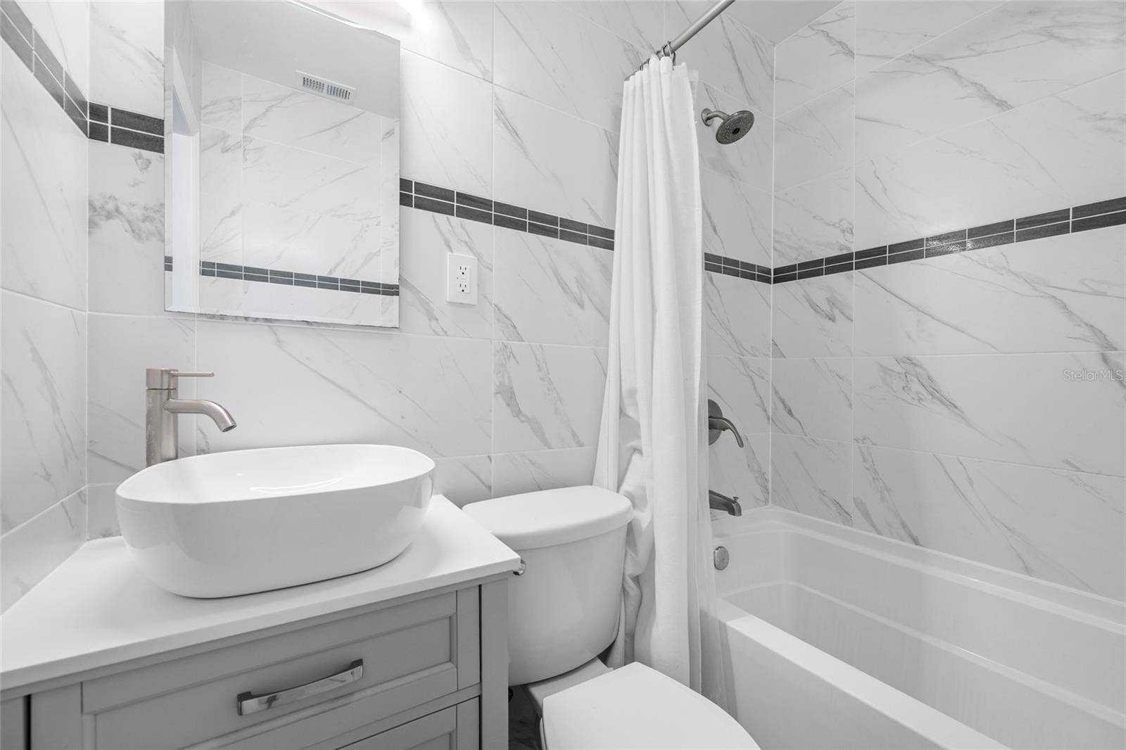 5044 BETTY STREET N, St Petersburg, FL 33709 Bathroom 2 features an upgraded vanity, marble tiles, and a bathtub with shower.