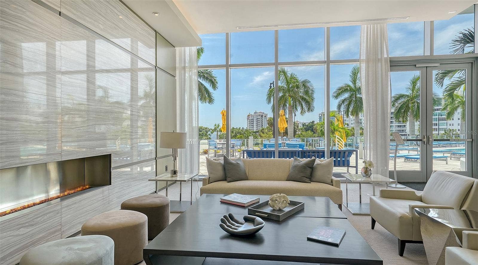 1155 N GULFSTREAM AVENUE, #207, Sarasota, FL 34236 An elegant lobby seating area framed by floor-to-ceiling windows overlooking the resort-style pool, offering a bright, inviting space to relax and enjoy the view.