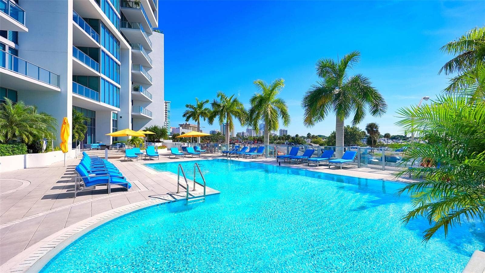 1155 N GULFSTREAM AVENUE, #207, Sarasota, FL 34236 A sparkling blue resort-style pool surrounded by an elegant sun deck with inviting lounge chairs and umbrellas, creating the perfect setting for relaxation and soaking up the Florida sunshine.