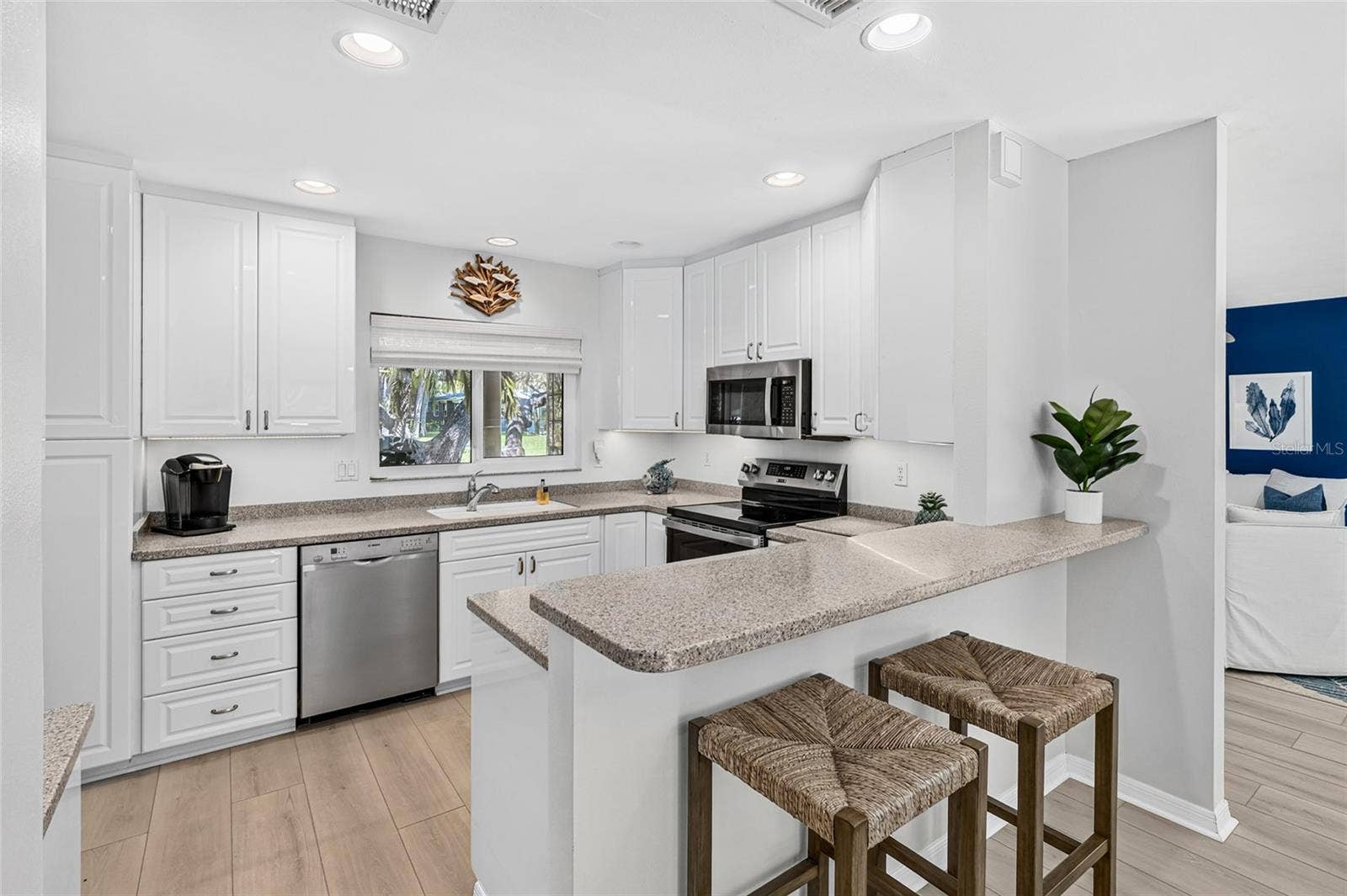Bright white kitchen offers generous cabinetry, stone counters, stainless appliances and plenty of gathering space.