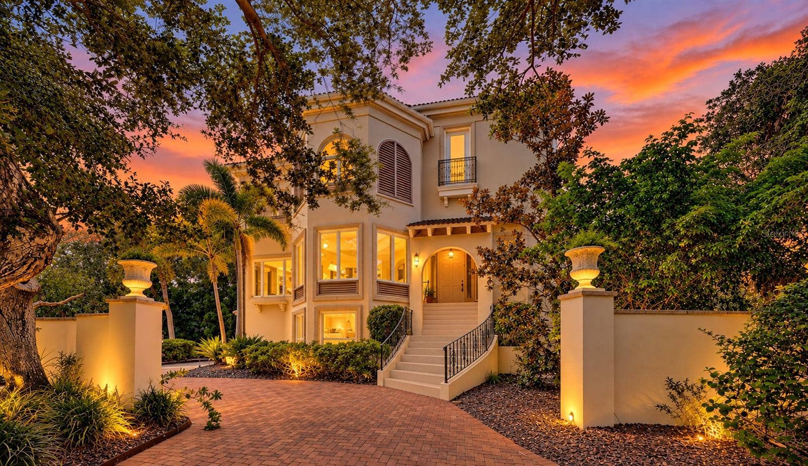 168 COASTAL HAMMOCK COURT, Osprey, FL 34229 Warm architectural lighting and mature oaks create a striking sense of arrival as evening falls.