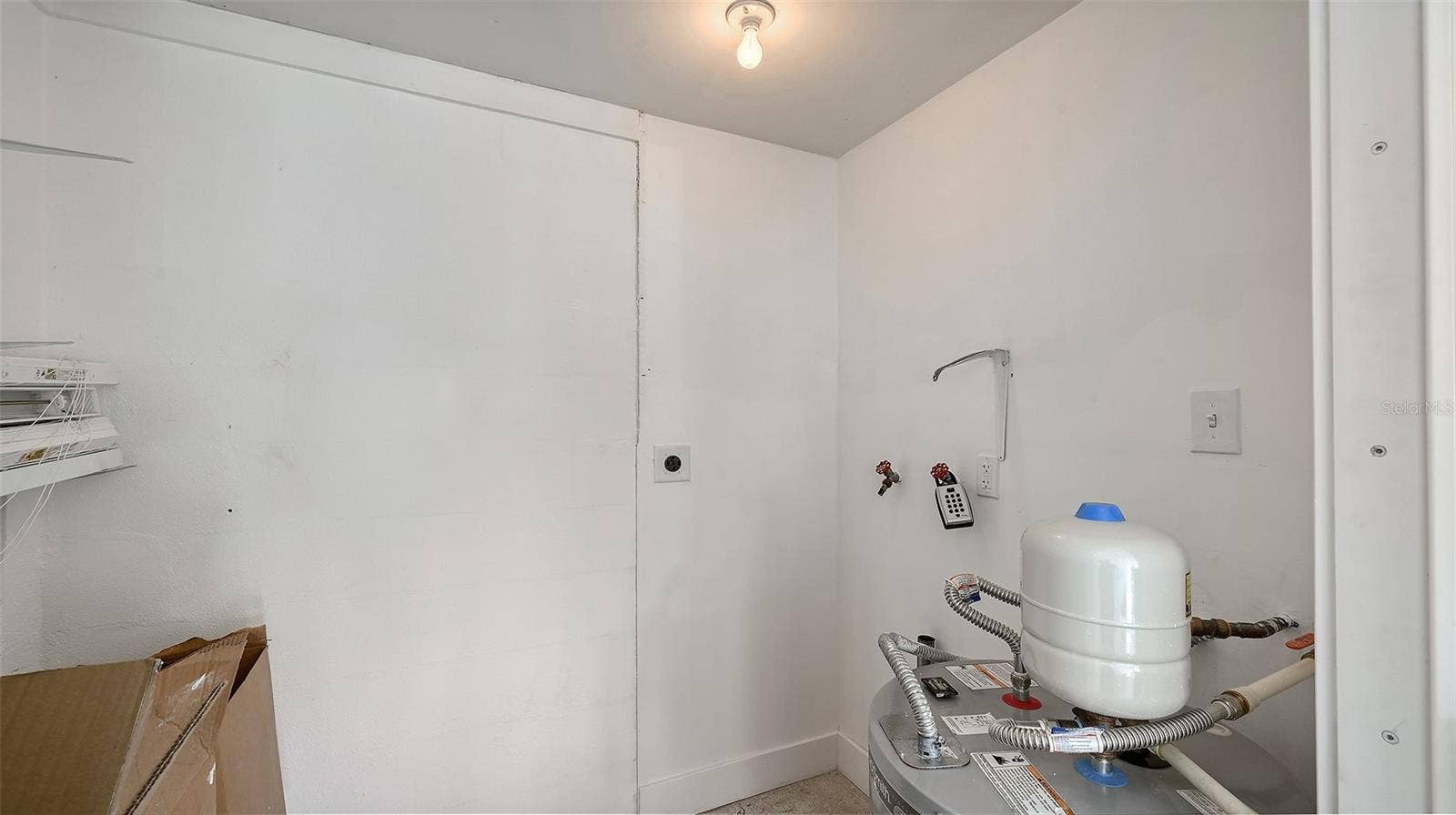 The storage room behind the carport with the new water heater and previous washer/dryer hookup.