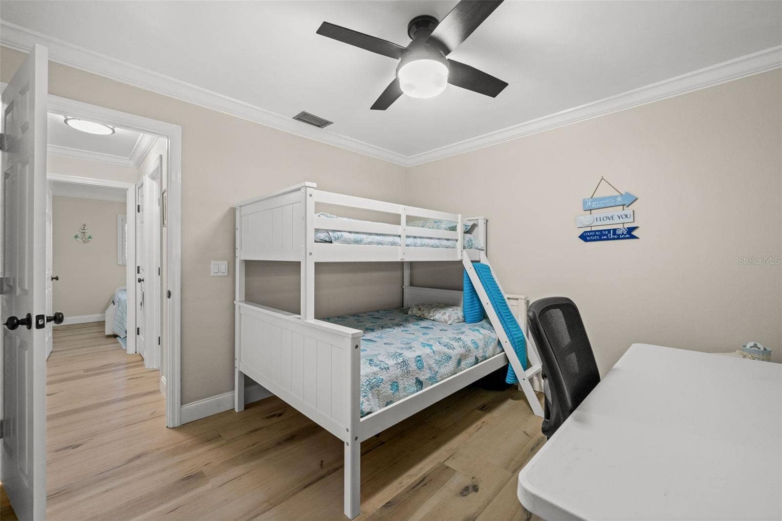 Neutral-toned interior featuring wood-finish flooring, crown molding, a central ceiling fan with integrated lighting, and white six-panel closet doors