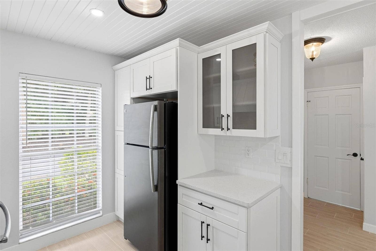 The opposite wall of the kitchen with pantry area, refrigerator and large window lending lots of natural light into the kitchen.
