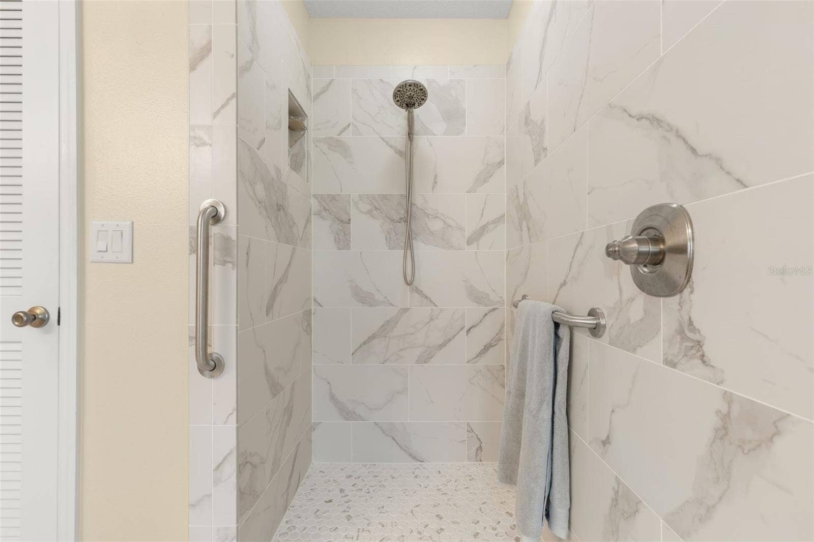 A closer look at the beautifully updated primary shower reveals striking tile, a pebble-style floor, built-in niche, and handheld showerhead, creating a refreshing escape with a touch of modern elegance.
