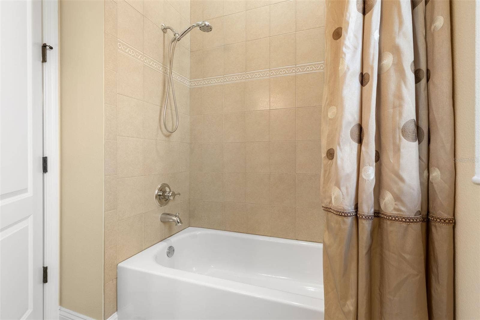 25 EMERALD LAKE COURT, Palm Coast, FL 32137 A closer look at the first-floor guest bathroom's tub/shower combination, featuring decorative tile accents and a handheld showerhead.