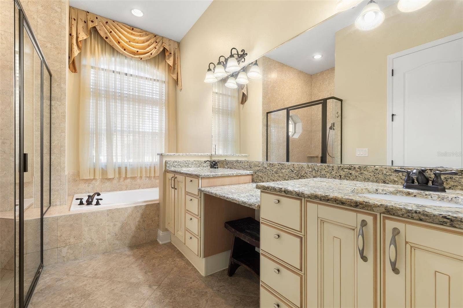 25 EMERALD LAKE COURT, Palm Coast, FL 32137 An Italian-inspired primary bathroom featuring dual vanities with granite countertops, a dedicated makeup area, soaking tub, and separate tiled shower.