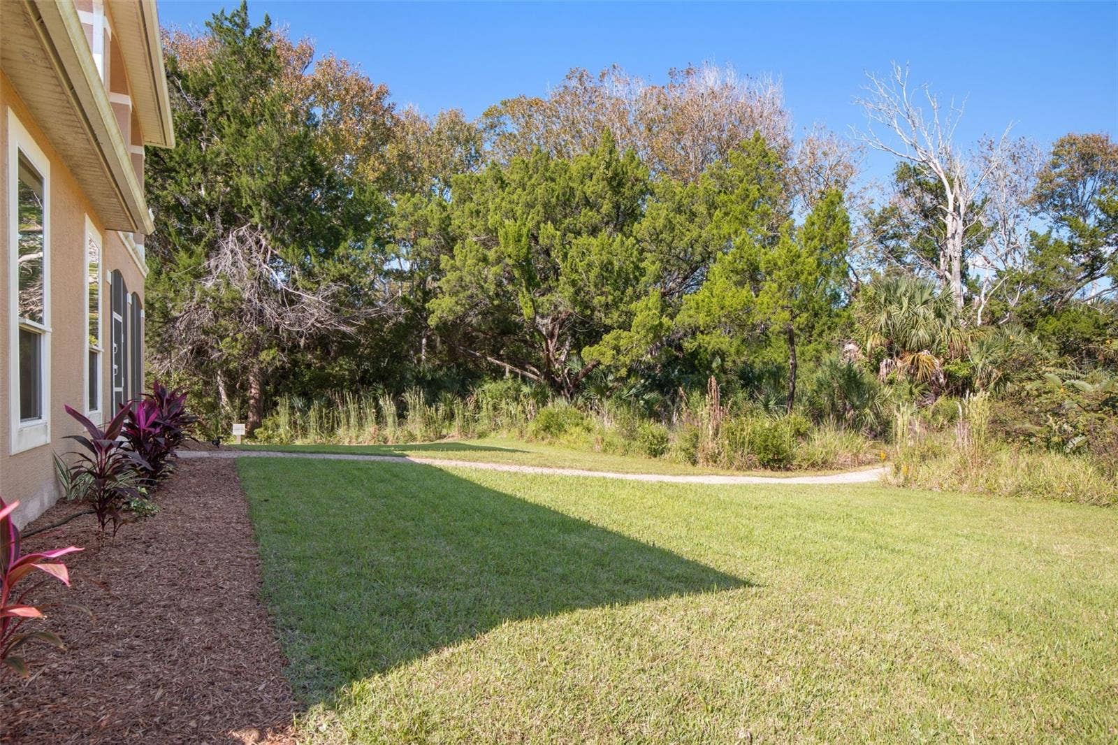 25 EMERALD LAKE COURT, Palm Coast, FL 32137 Peaceful backyard surrounded by natural greenery with a walkway leading toward Emerald Lake.