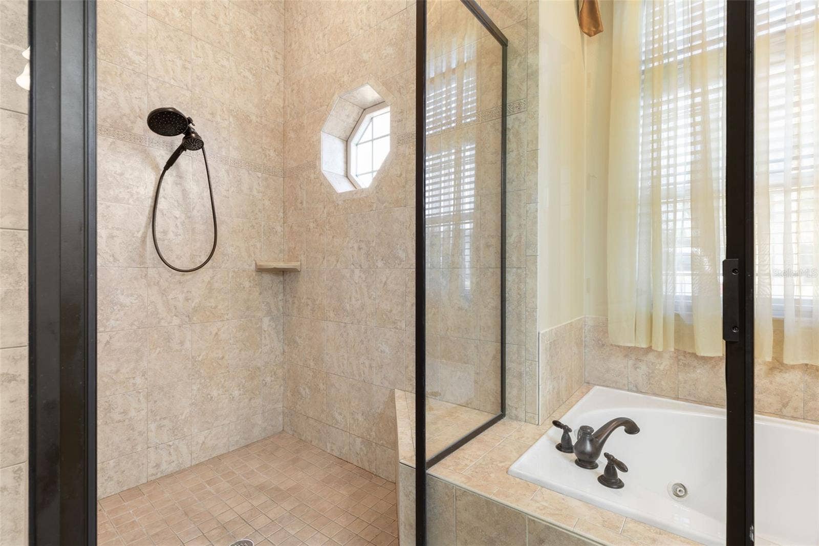 25 EMERALD LAKE COURT, Palm Coast, FL 32137 A spacious, tiled walk-in shower featuring glass enclosure, handheld showerhead, and a distinctive octagonal window.