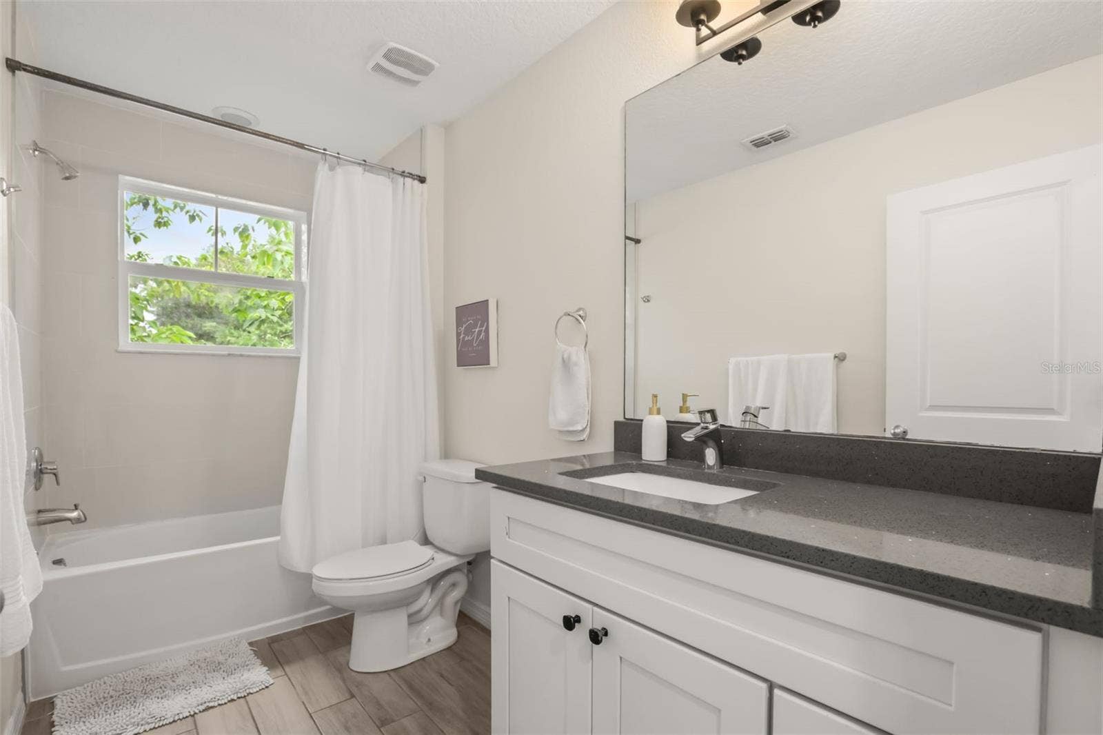 Bright guest bathroom featuring a single vanity, tub/shower combination, and a functional layout.