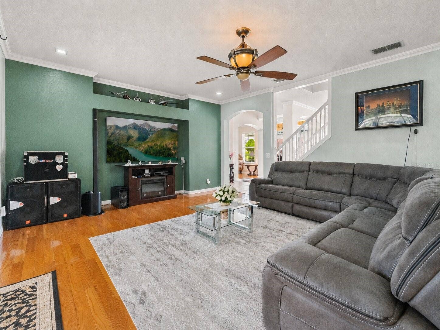 211 HUNT STREET, Clermont, FL 34711 Family room with accent wall, wood flooring, ceiling fan, and generous gathering space.